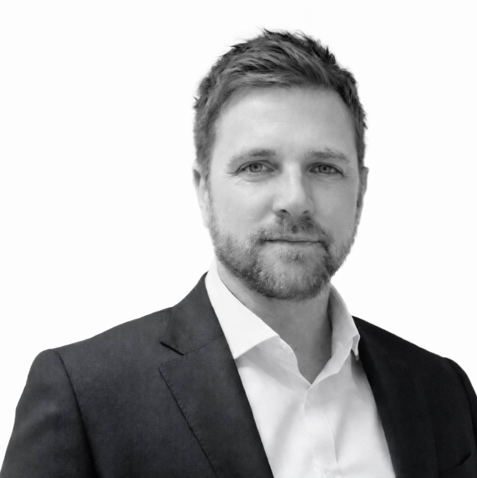Black-and-white photograph of a man wearing a dark suit and collared shirt, with a beard and short, styled hair.