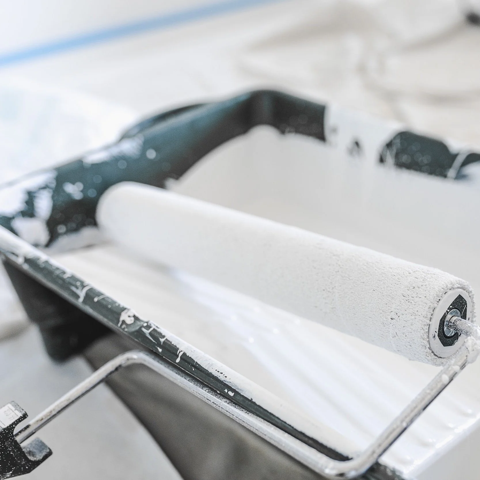 Close-up of a paint roller covered in white paint resting in a paint tray with some spilled paint around.