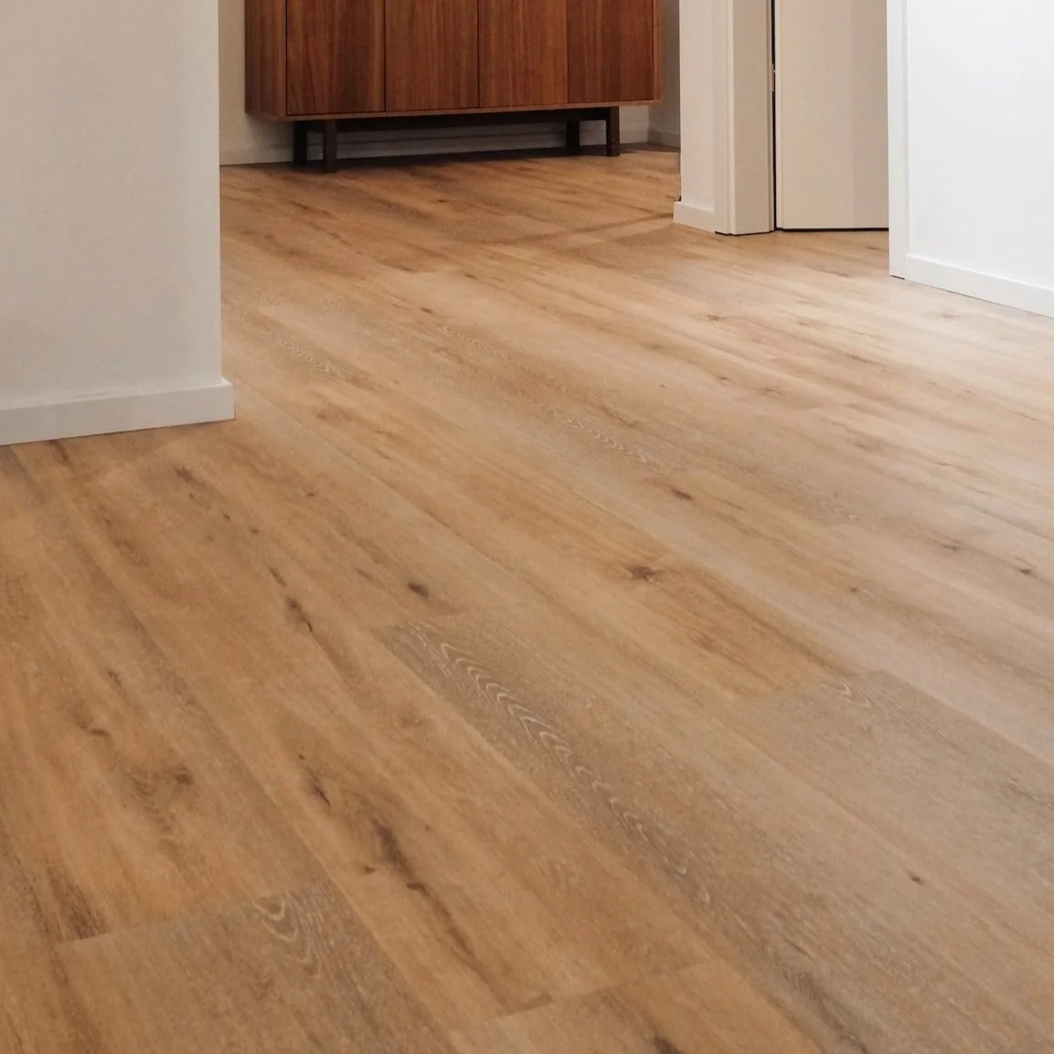 Smooth light brown hardwood floor in a room with a white wall and wooden cabinet.