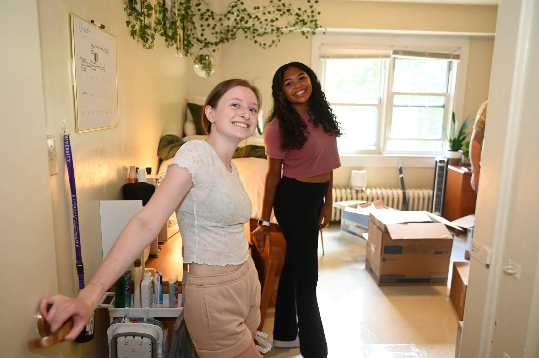 Two new roommates pose for a photo at the door of their dorm room