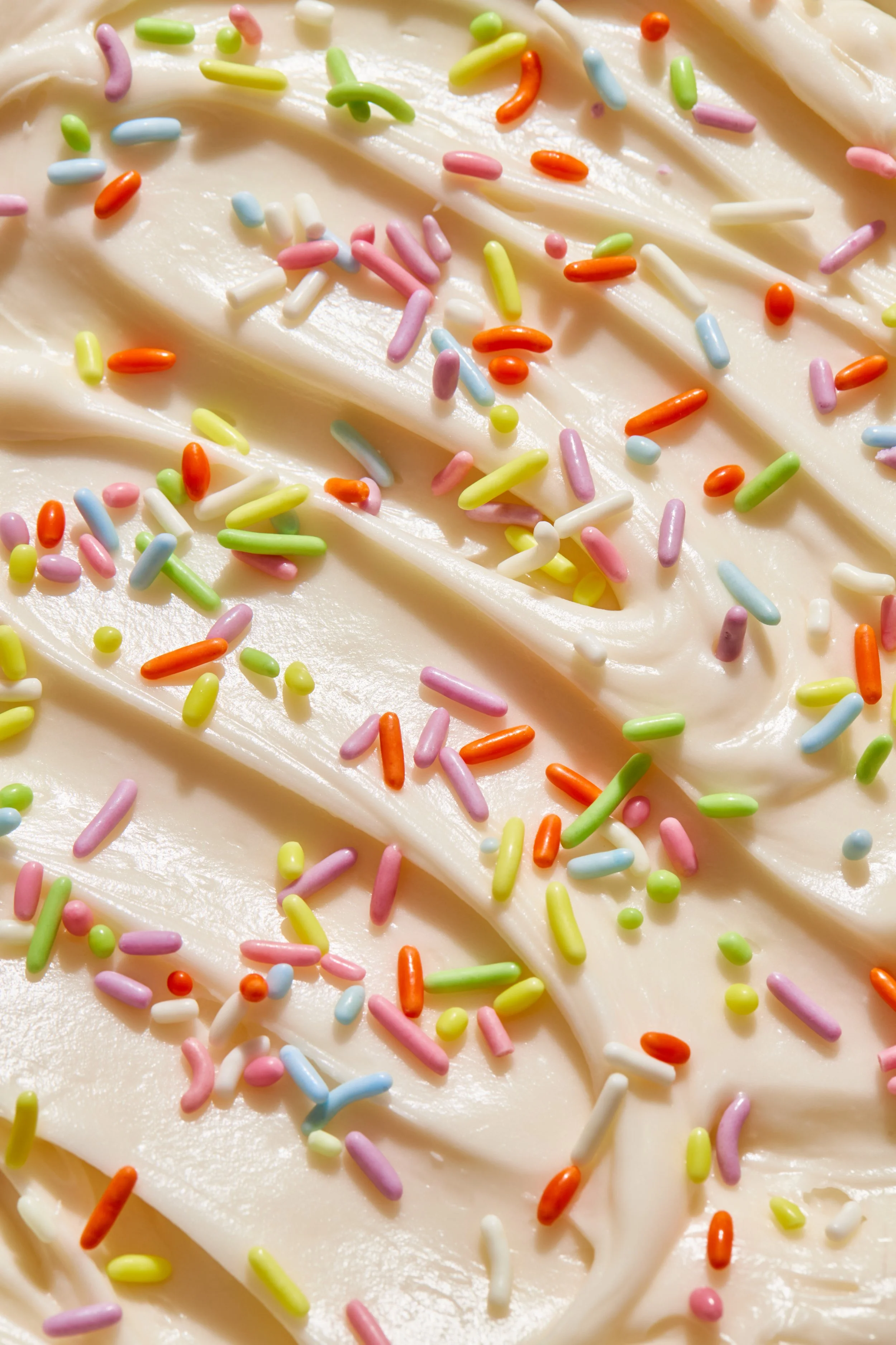 Close-up of vanilla frosting with colorful rainbow sprinkles on top.