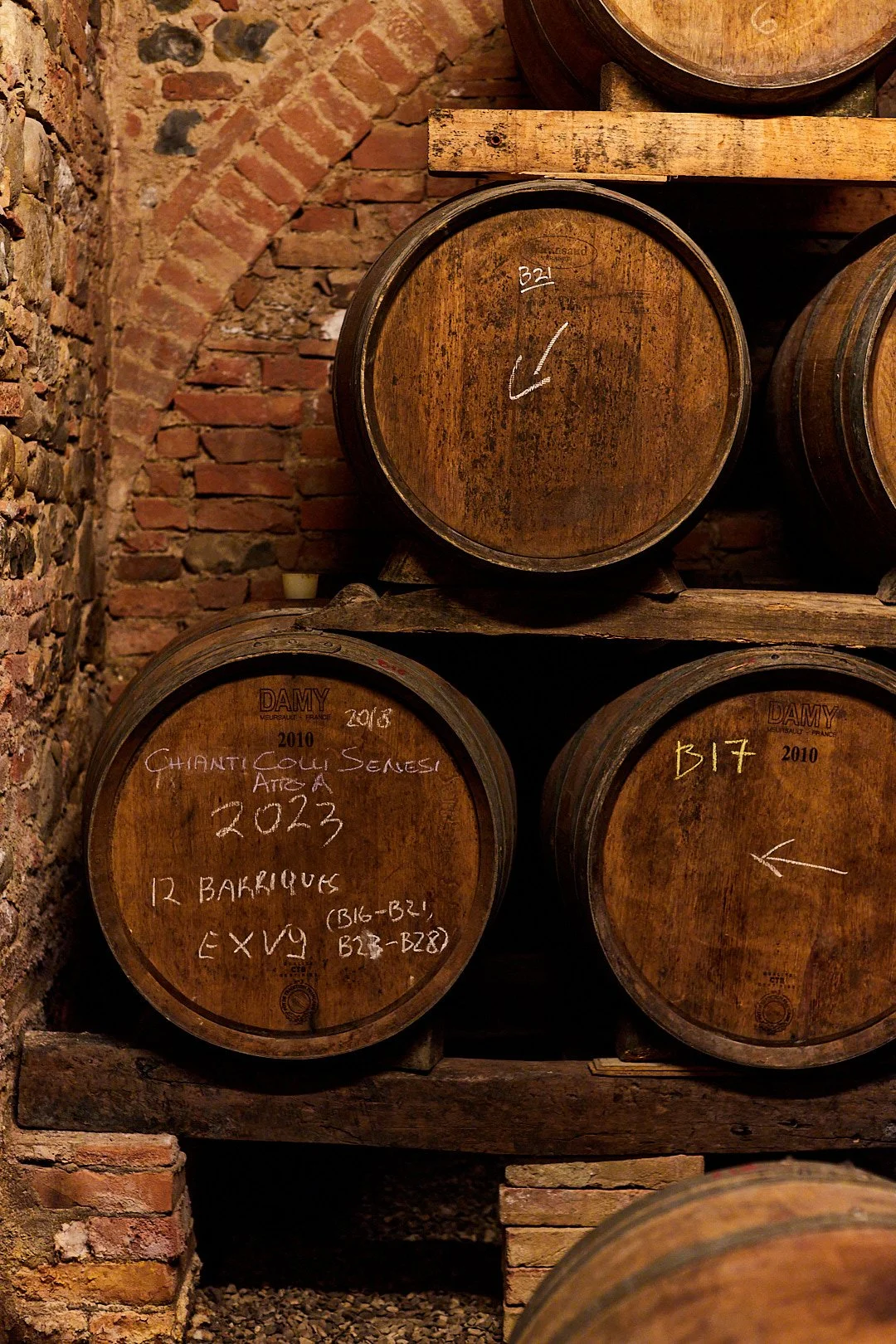 Wine barrels stored in a cellar with brick walls, marked with vintage years and tasting notes.