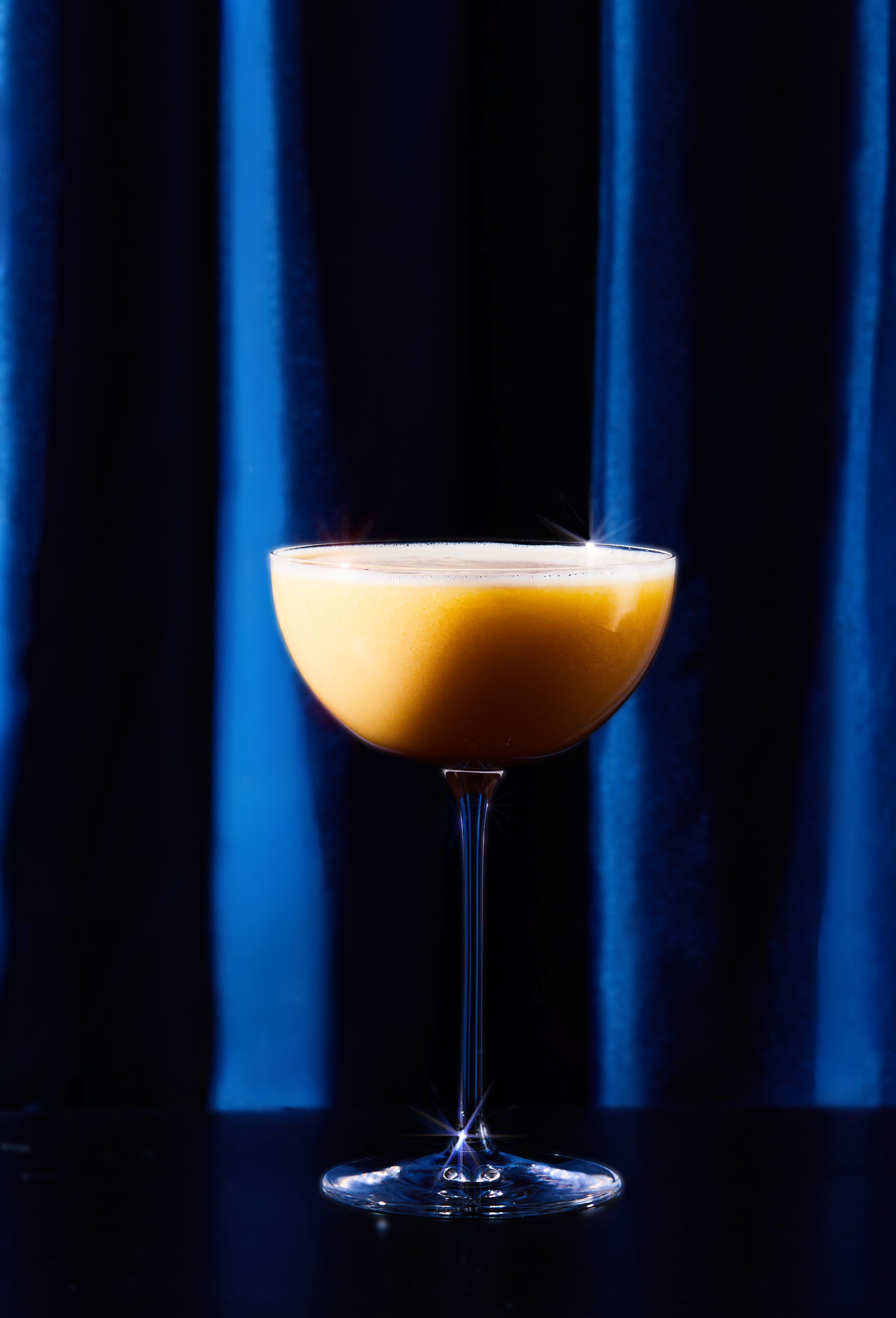 Picture of cocktail with dramatic lighting against a blue curtain