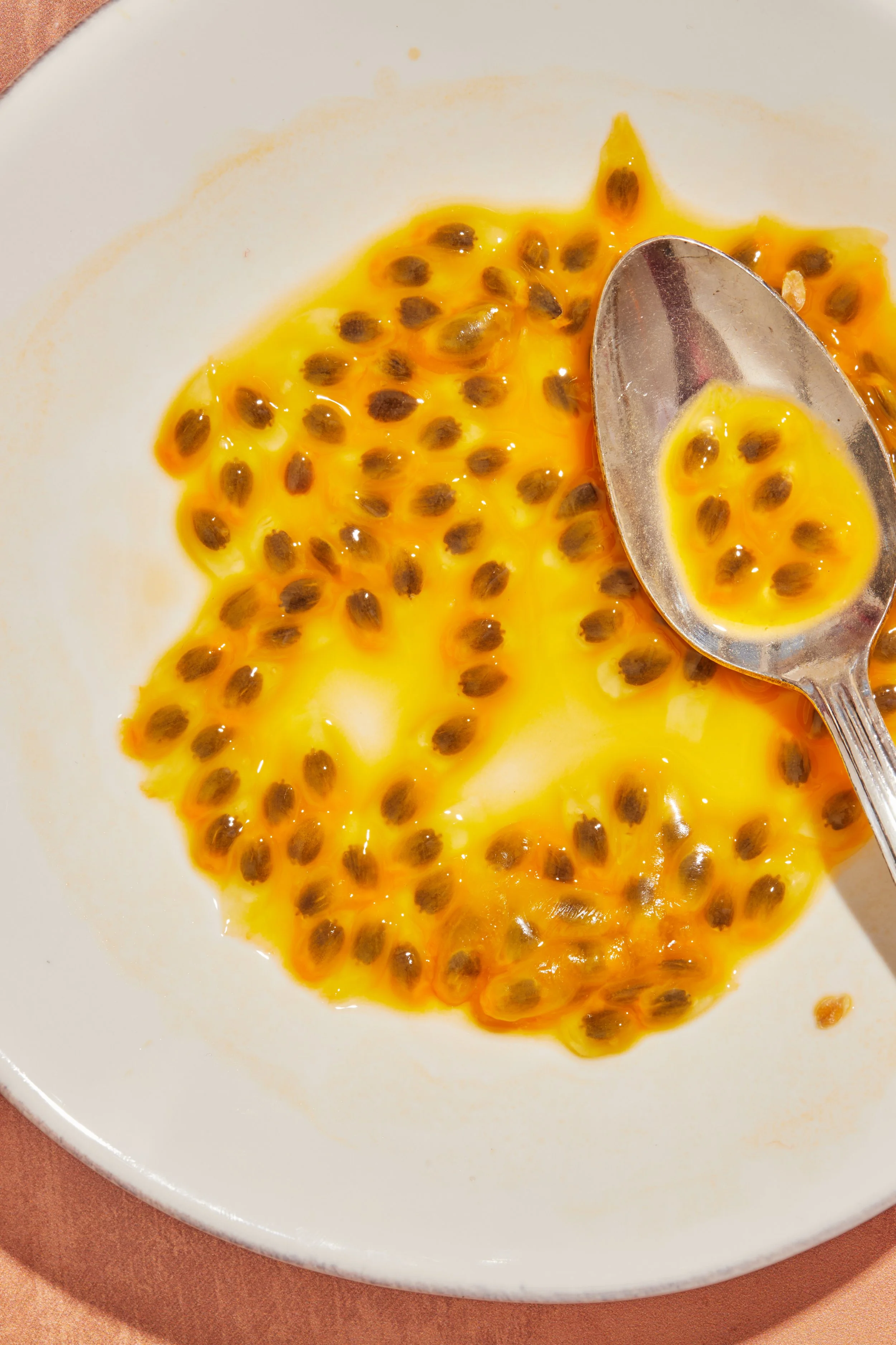 Passion fruit pulp with black seeds on a white plate with a spoon.