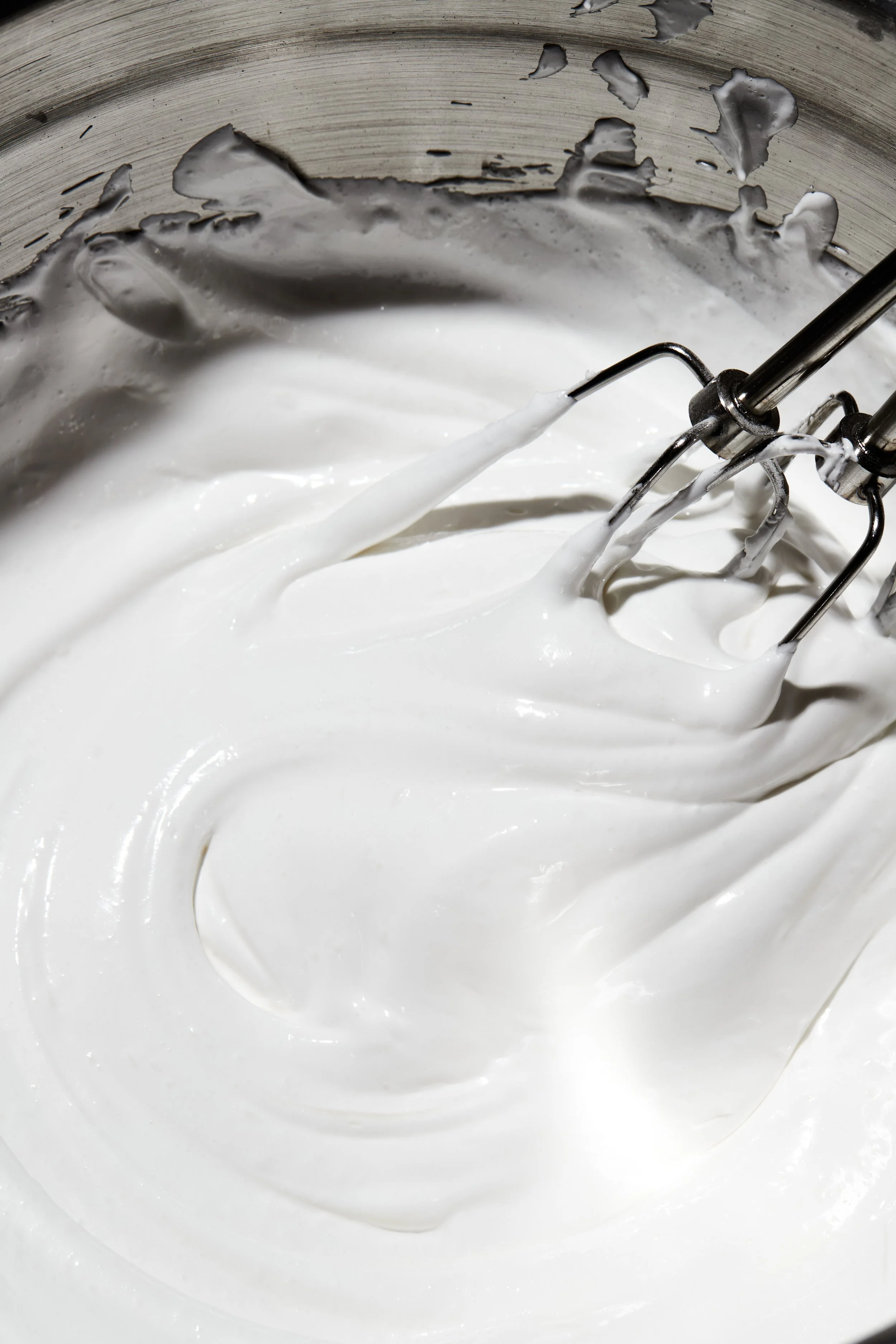 Close-up of a mixer beating white whipped cream in a metal bowl.