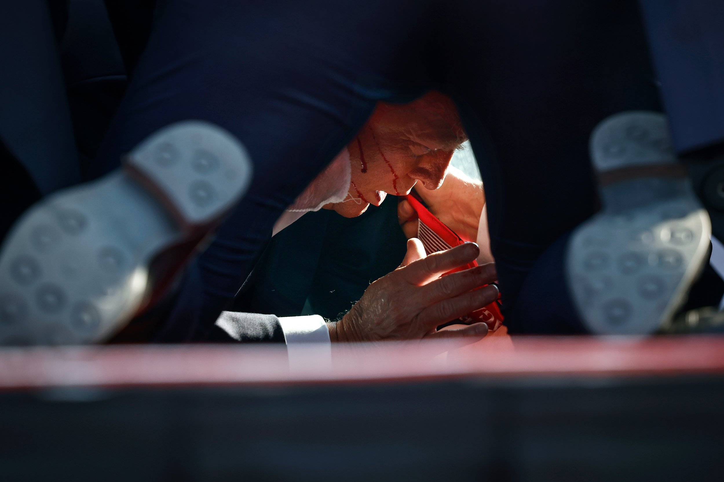 (photo by Anna Moneymaker/Getty Images) Butler, Pa., July 13, 2024: Secret Service agents cover Republican presidential candidate Donald Trump as he lies on the ground bleeding after he was shot during a campaign rally.