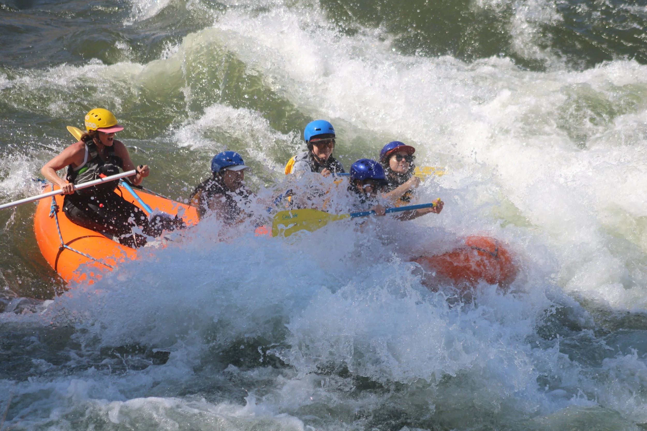 Two people wearing helmets and life vests white water kayaking in a river with rocks.