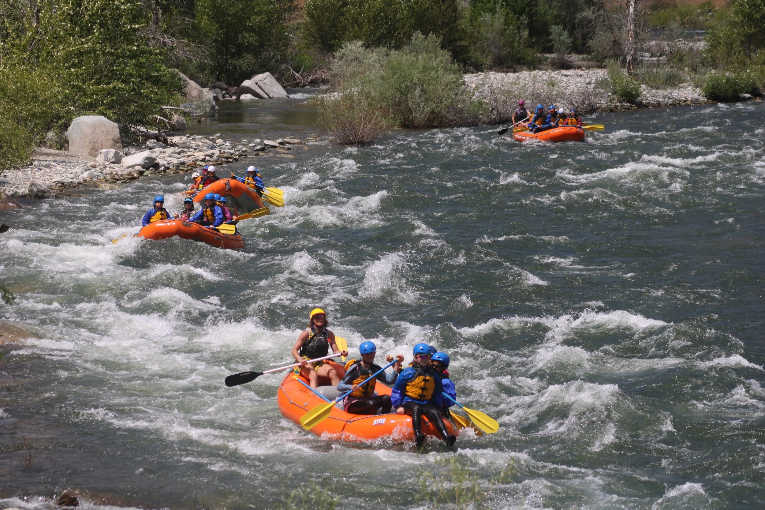 Group of people white water rafting on a river, wearing helmets and life jackets, splashing water.