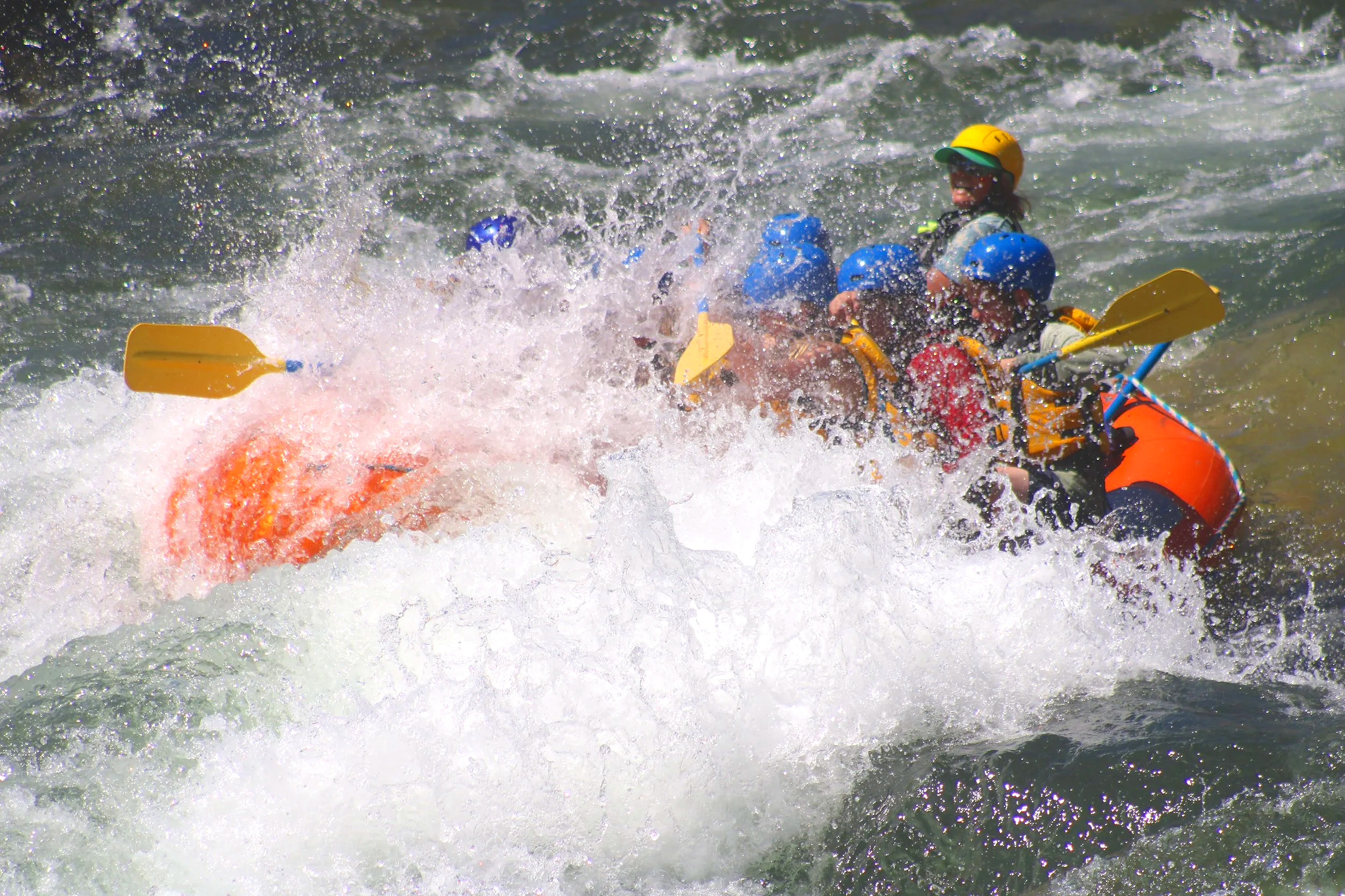 Group of people white water rafting in river, wearing life jackets and helmets.