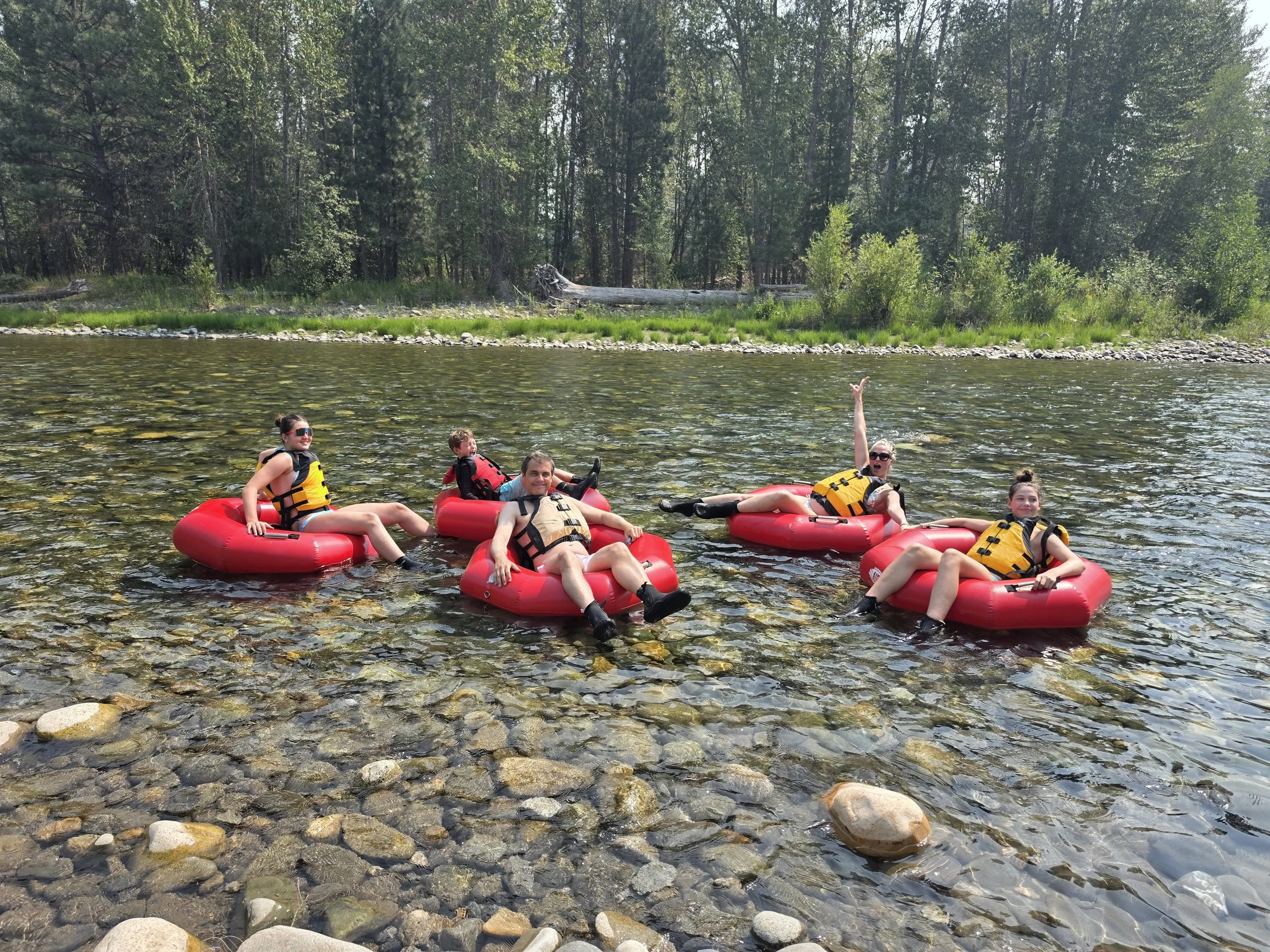 People floating down a river on red inner tubes on a sunny day with trees and a blue sky in the background.