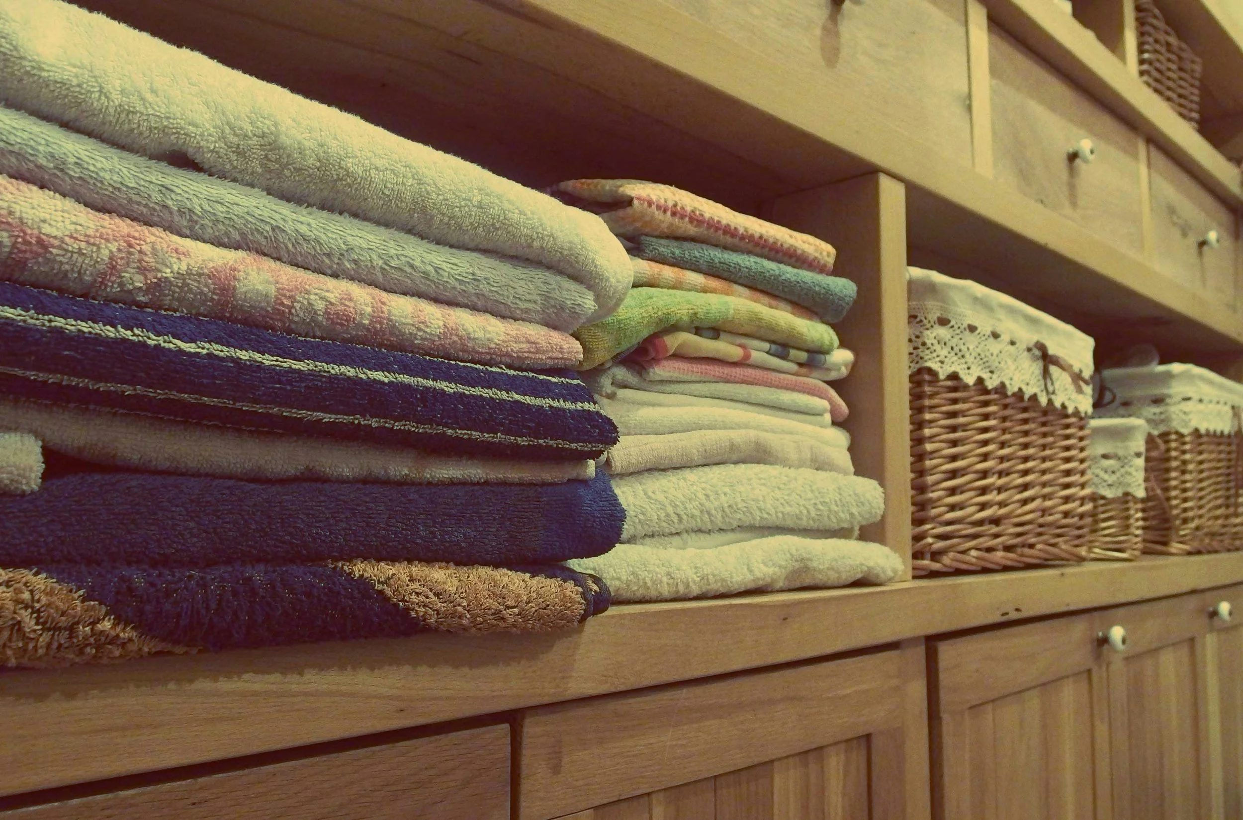 Neatly folded towels and woven baskets on wooden shelves in a well-organized linen closet.