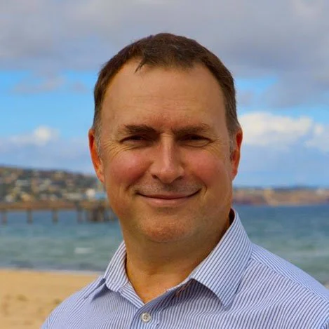 Stuart Roe from ETG Wealth on a beach with the ocean and cloudy sky in the background.
