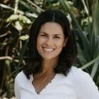 Financial Adviser Lisa Kirk from Fuse Wealth with shoulder-length dark hair smiling outdoors, surrounded by green foliage.