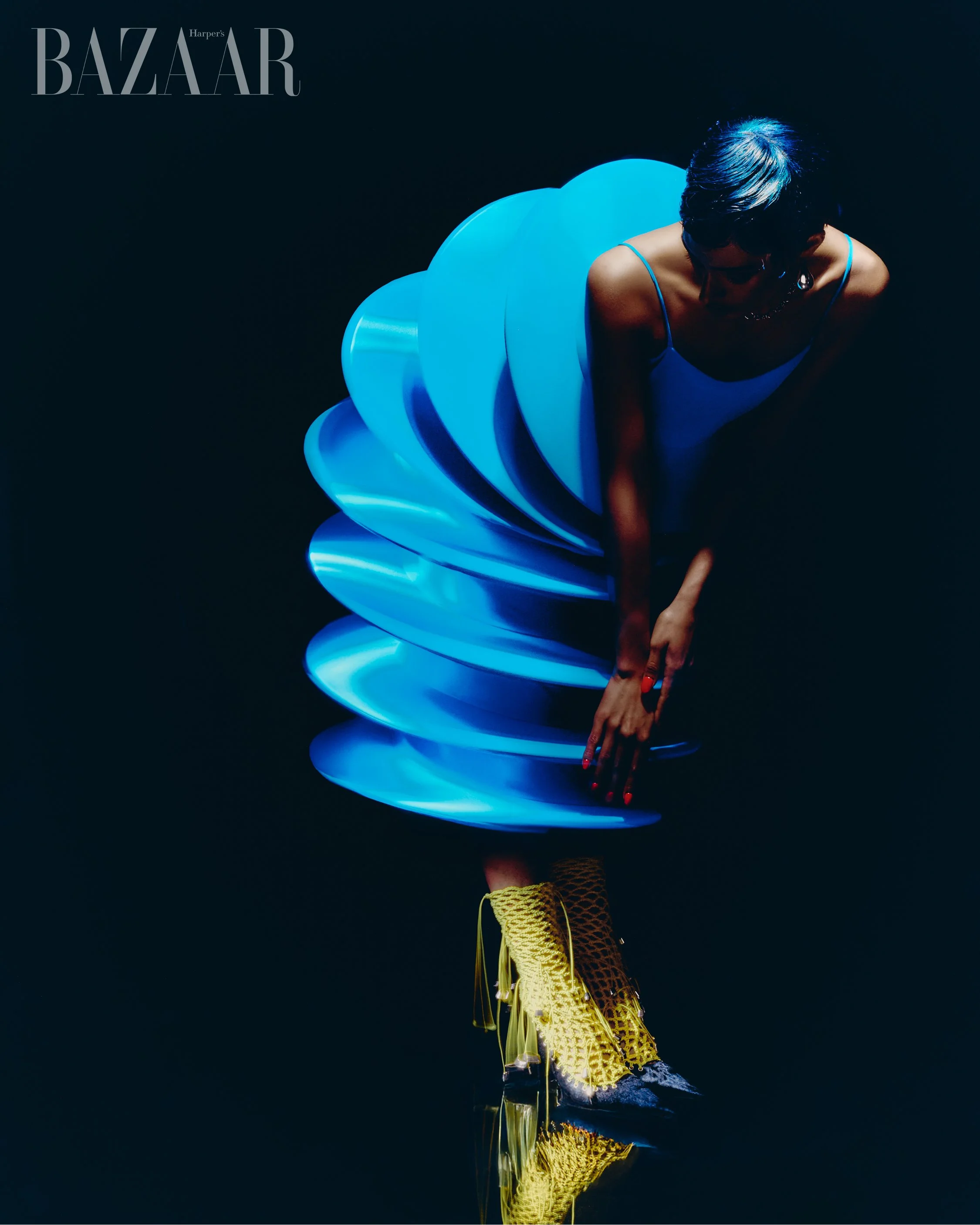 Harpers Bazaar editorial portrait featuring model in sculptural blue dress with dramatic lighting and reflective floor photographed by Radhika Muthanna