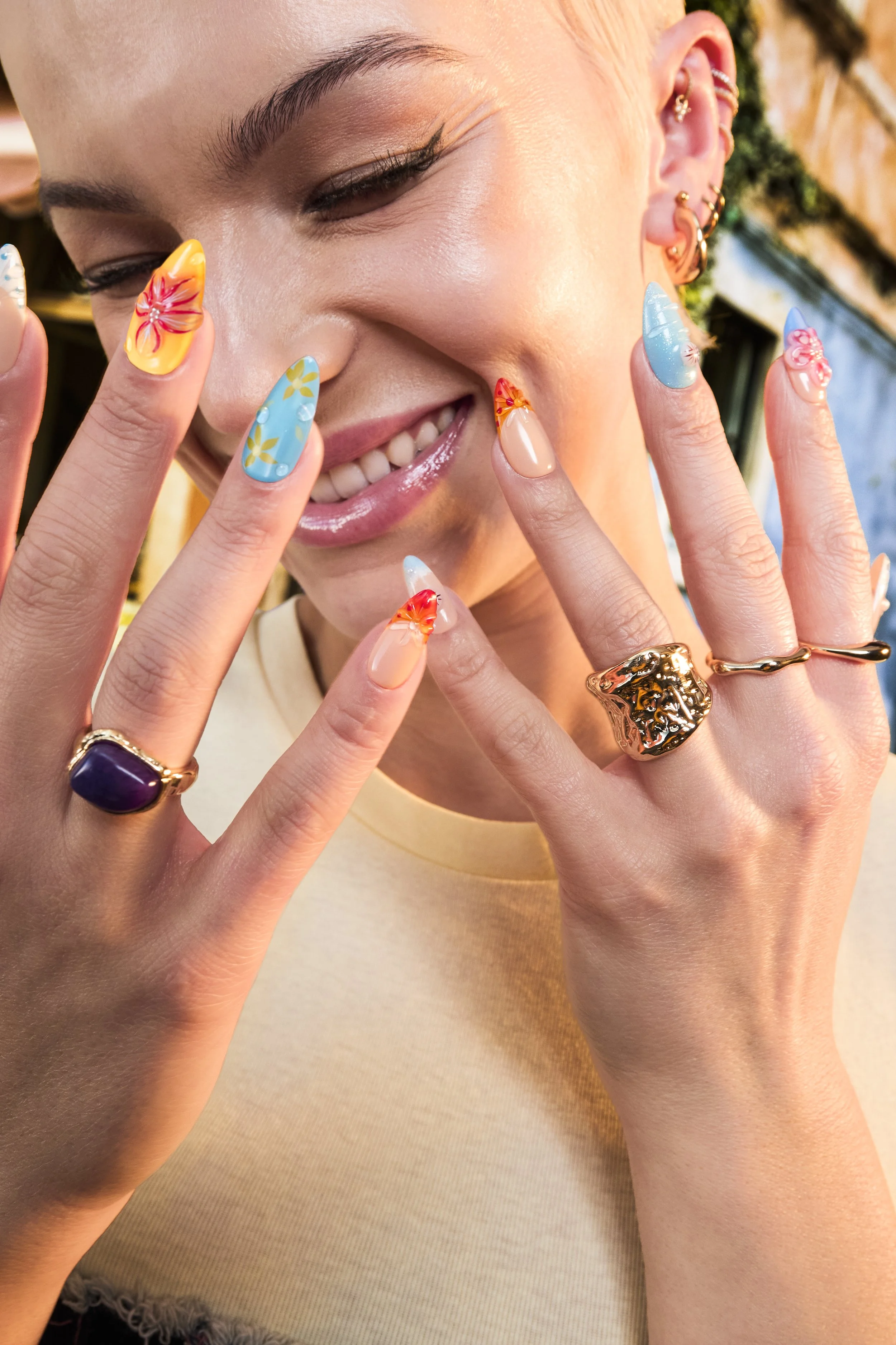 Beauty editorial portrait of a blonde model with colourful floral nail art and gold jewellery in warm summer sunlight.