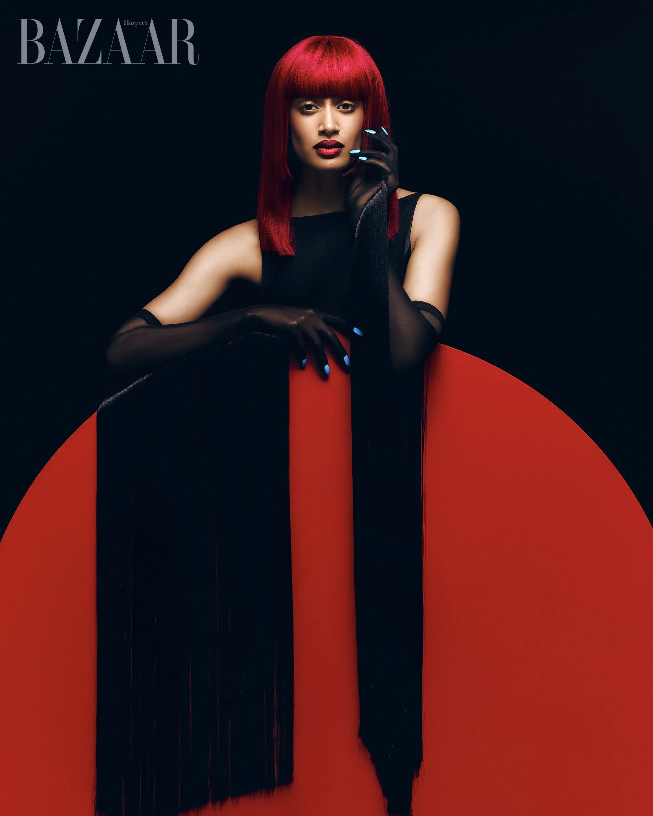 Harpers Bazaar editorial portrait featuring model with red hair in black sculptural dress against dark background photographed by Radhika Muthanna