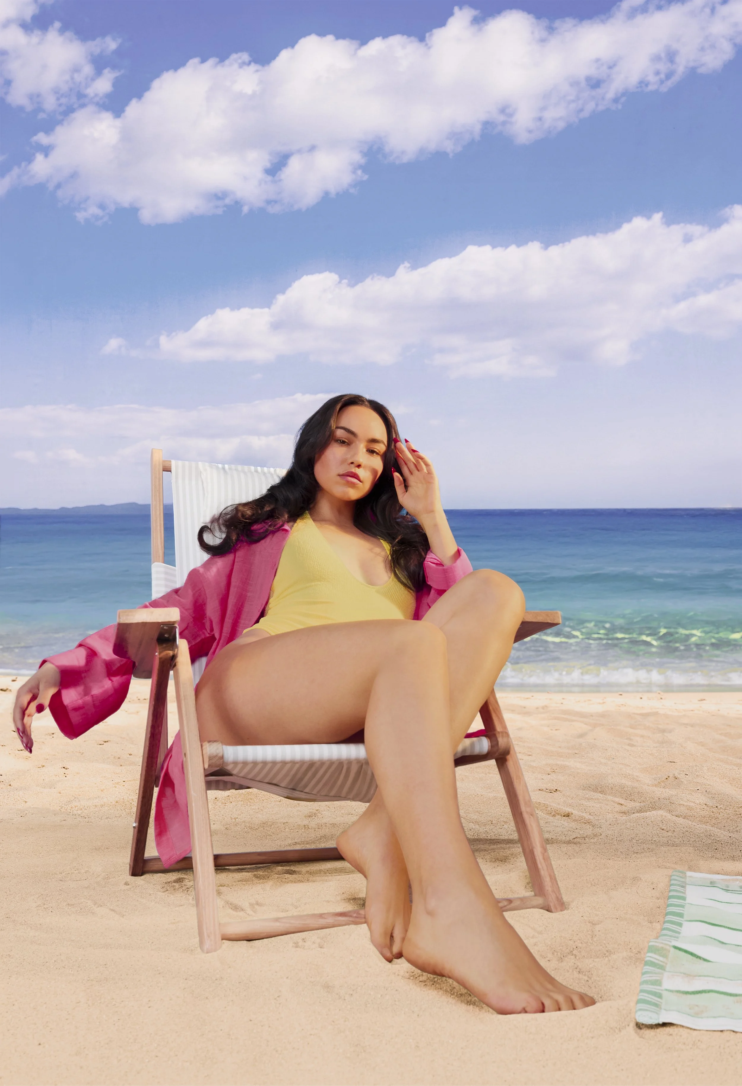 Brunette model in bright pink and yellow resort wear photographed on a beach for a colourful summer fashion editorial.