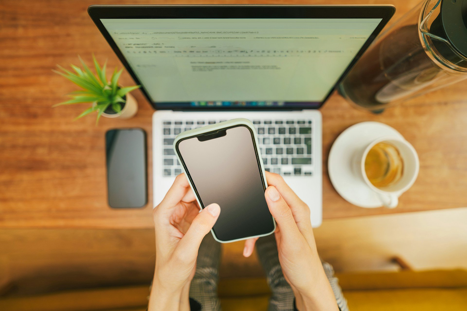 A person doing a search on their phone while having a coffee and her laptop next to her