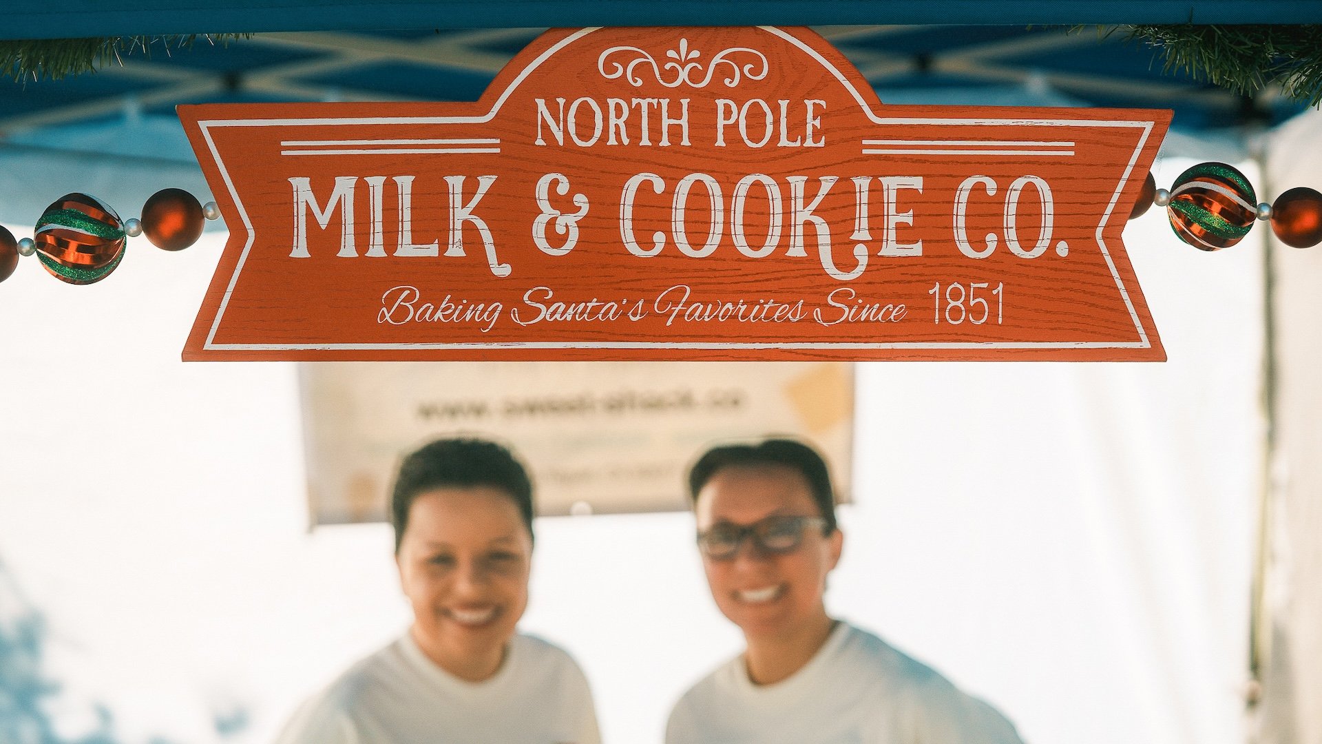 Two happy business owners posing proud next to their business sign