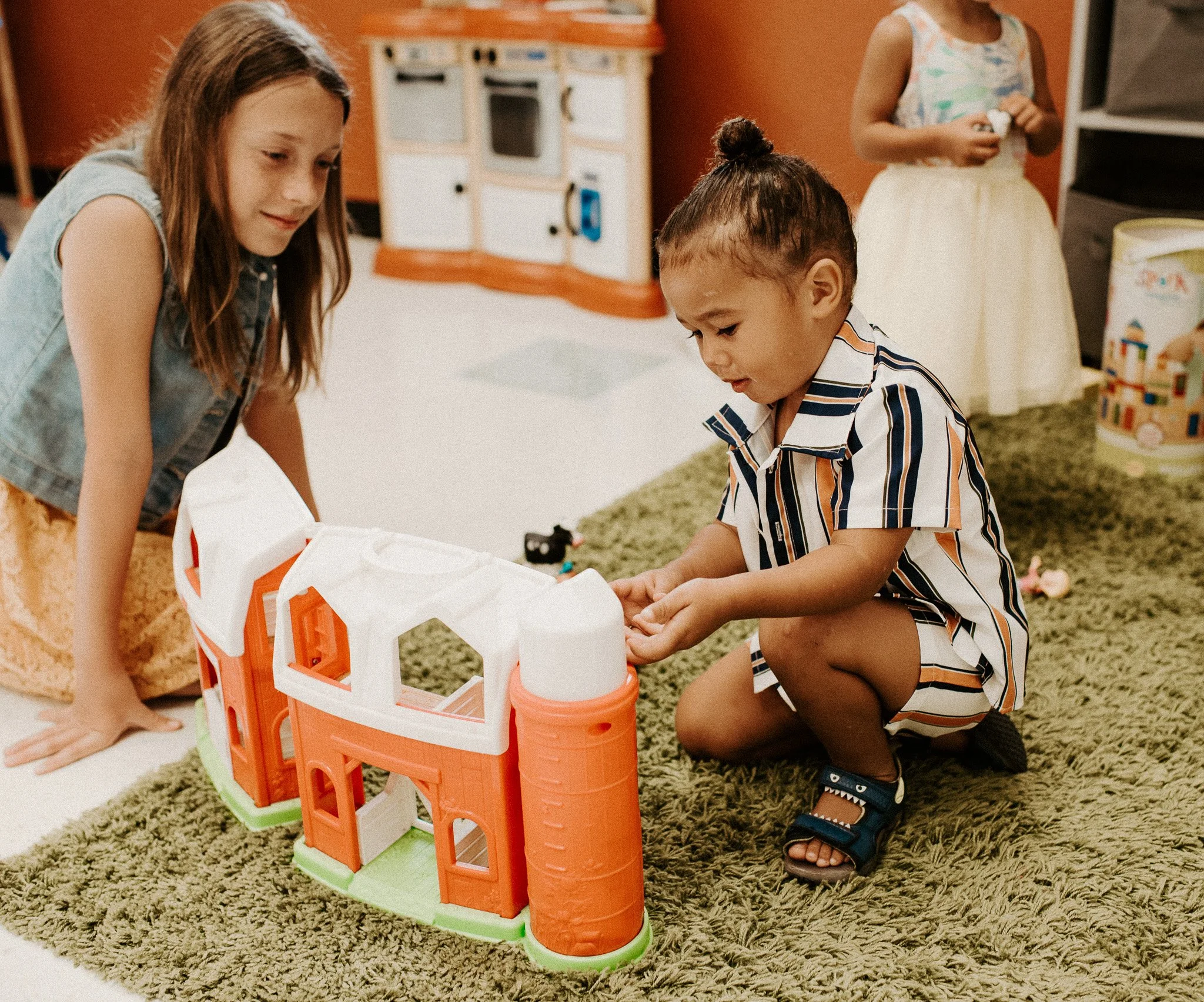 young girl playing at dollhouse with young child