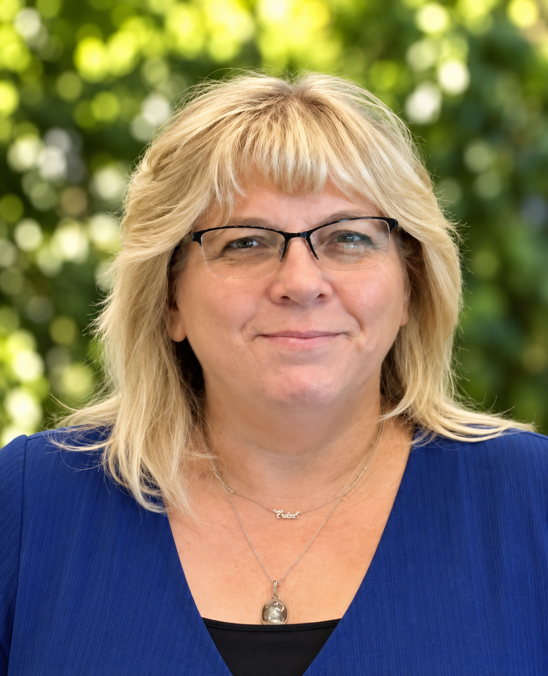 A woman with blonde hair wearing glasses and a blue top.