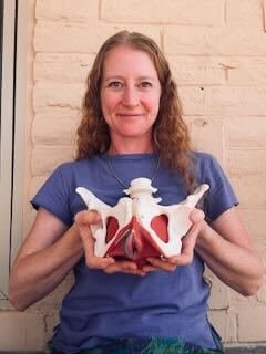 Siri Garfinkel, a myofascial release therapist in Tucson, Arizona, holding a model of a human pelvis and lower spine against a brick wall
