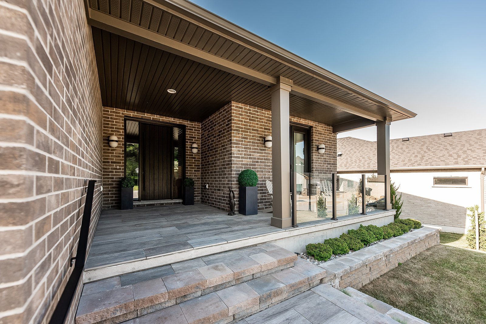 Modern brick house entrance with steps, planters, and glass railing.