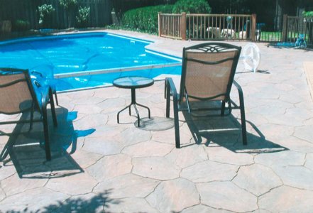 Backyard swimming pool with lounge chairs and a small table on a stone patio.
