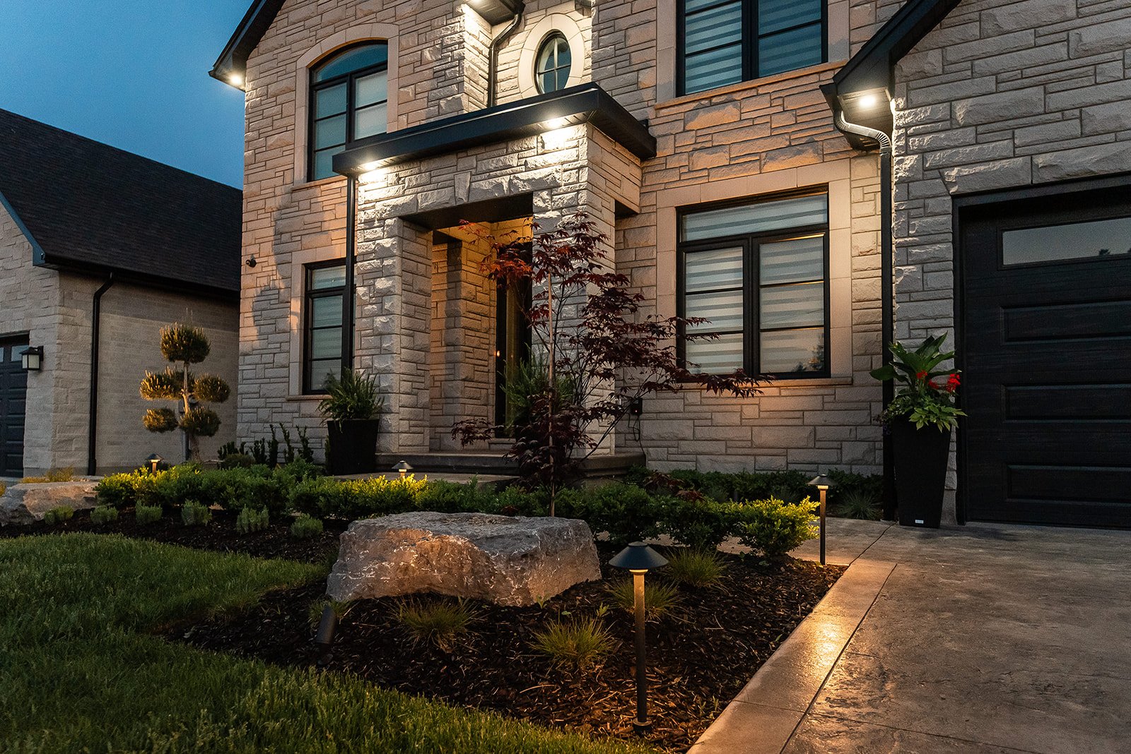 Elegant modern brick house with outdoor lighting, landscaped garden, and stone pathway at dusk.