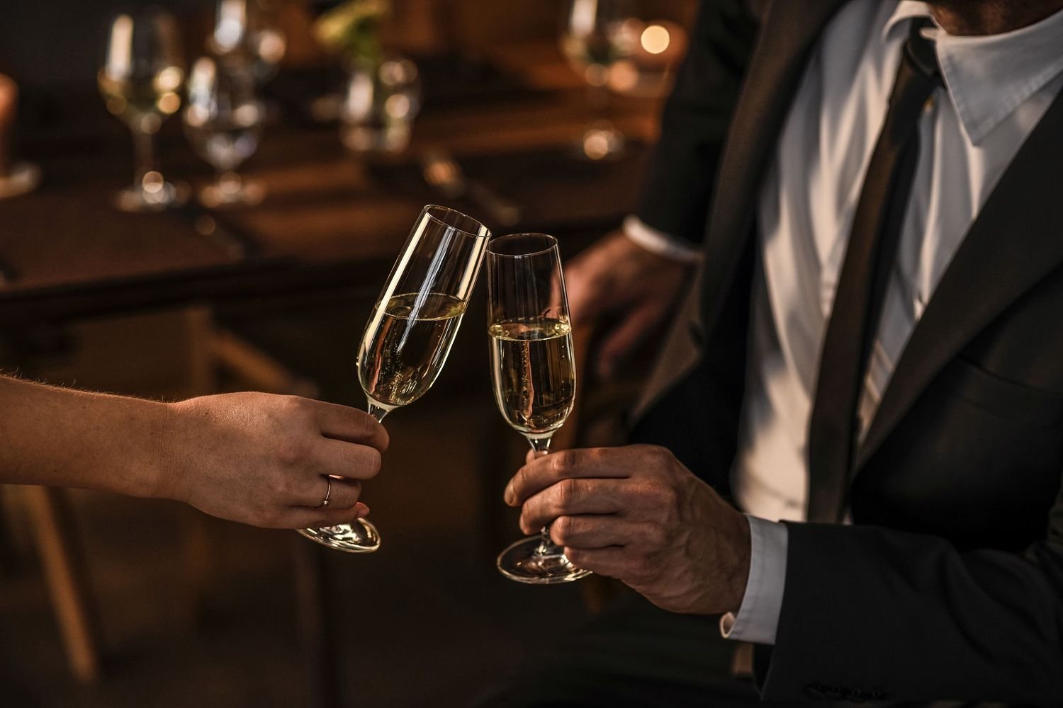 Two people clinking champagne flutes filled with sparkling wine or champagne at a celebration or romantic event.