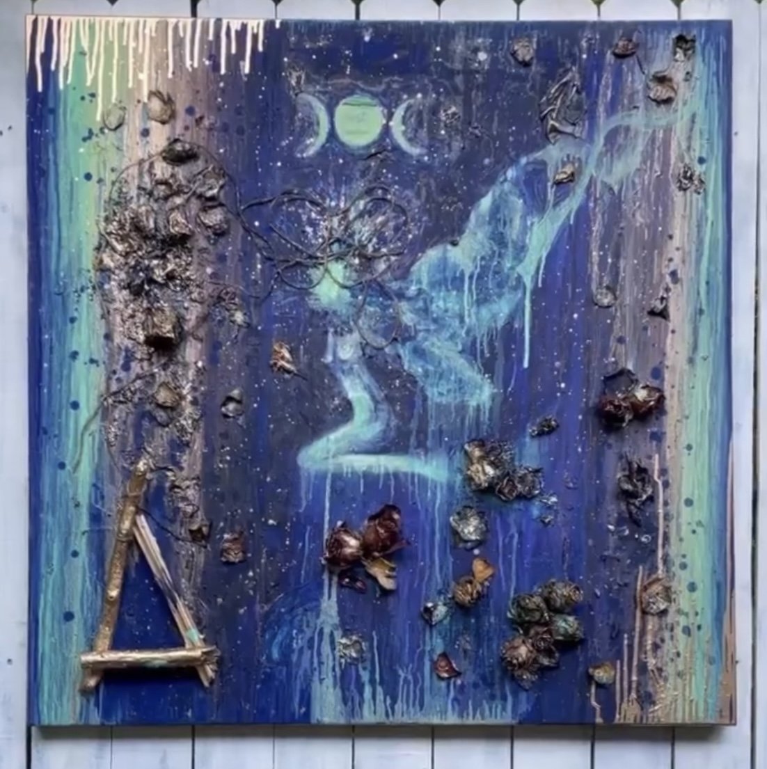 Mixed media art piece featuring a human face silhouette with a starry night sky, planets, and flowing colors, decorated with rocks, driftwood, and natural elements.