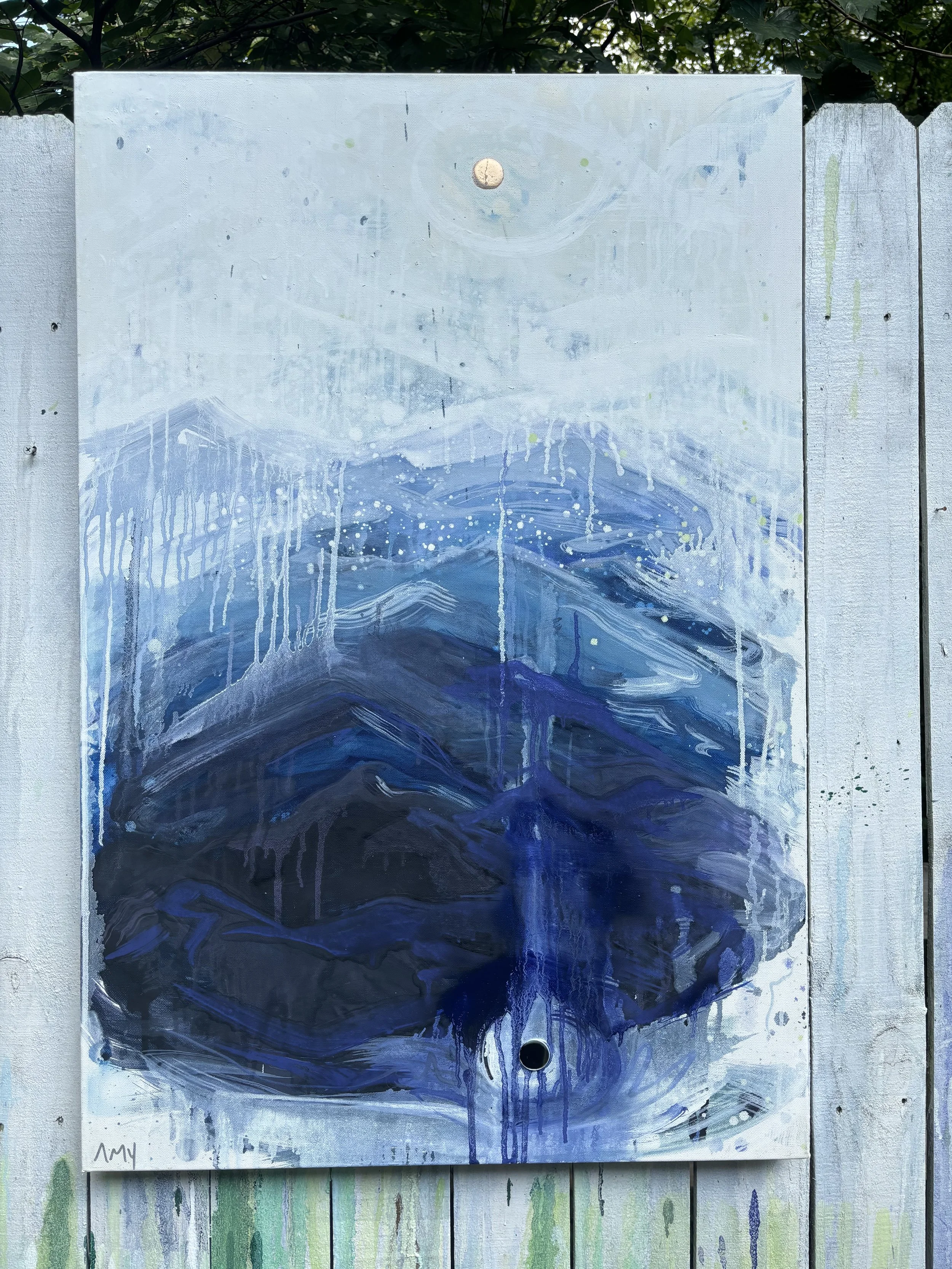 Painting of mountains and water in shades of blue and white, with dripping paint effects, mounted on a wooden fence.