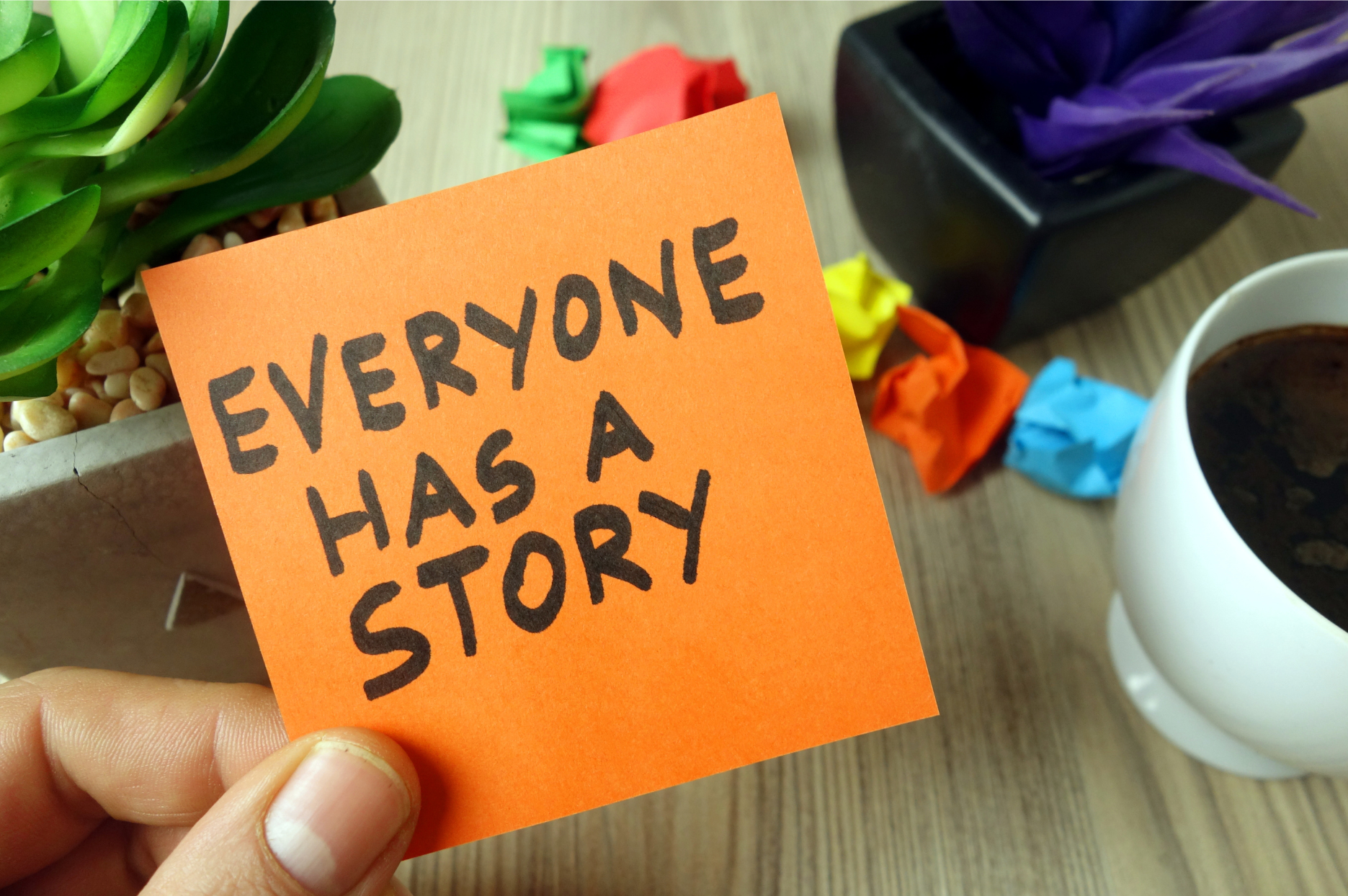 hand holding an orange post-it note that reads Everyone Has a Story