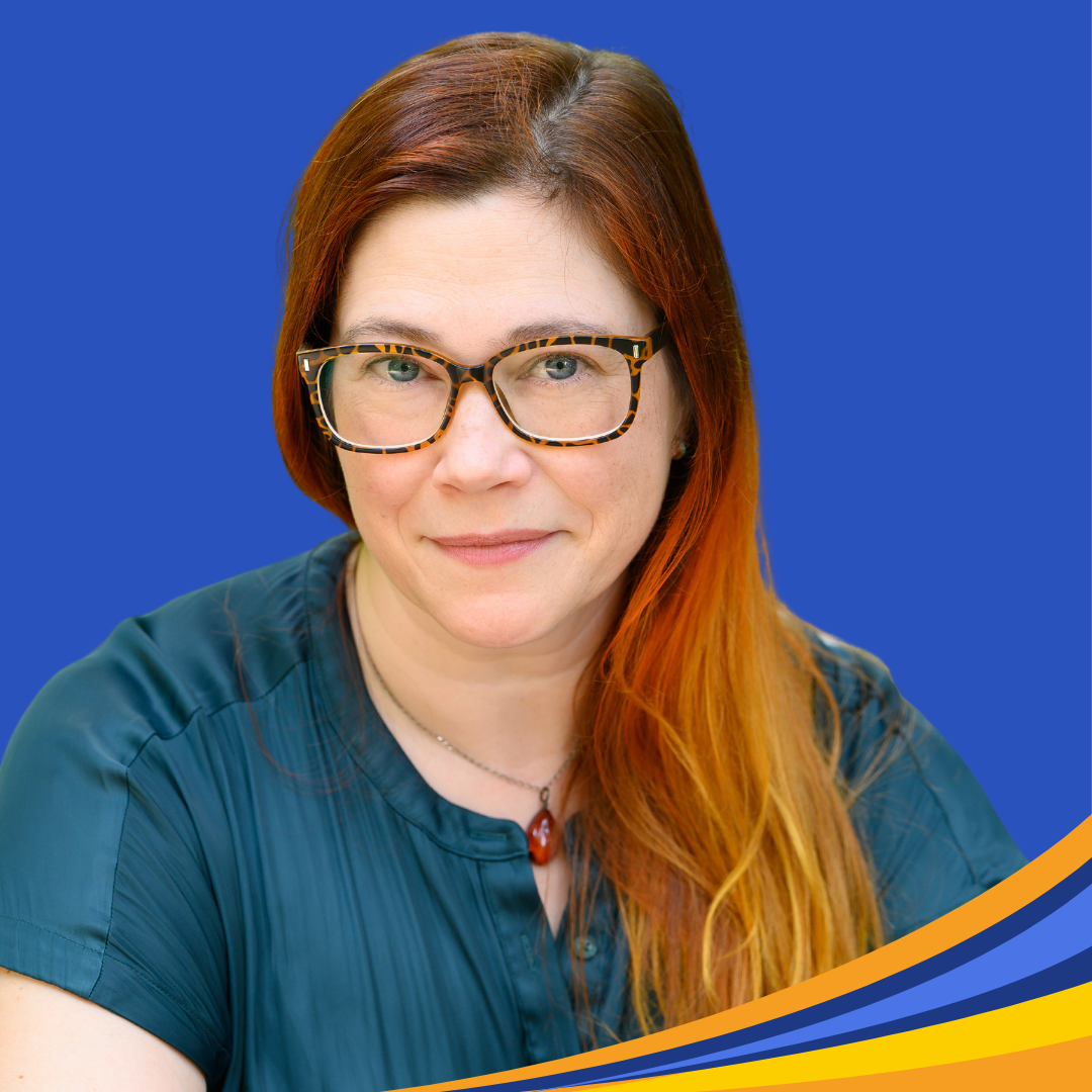 Smiling woman with brown rimmed glasses and long red, orange, and yellowhair