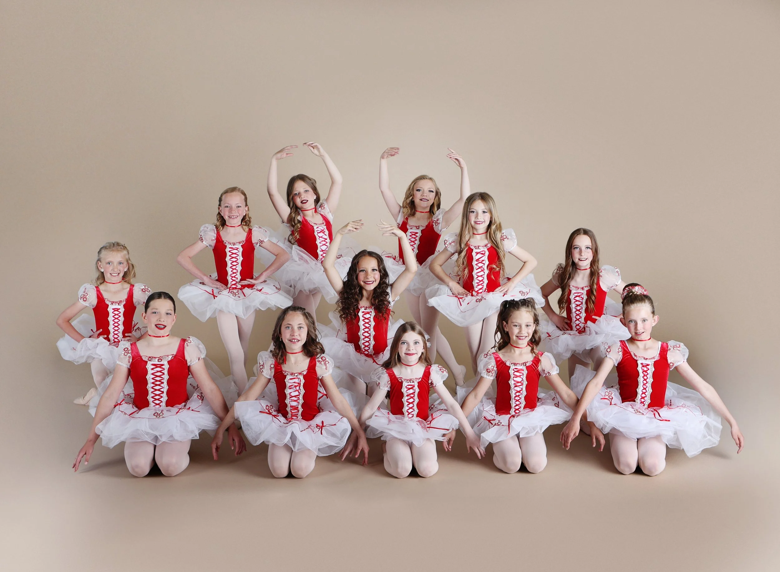 Group of young girls dressed in red and white ballet costumes posing against a beige background.