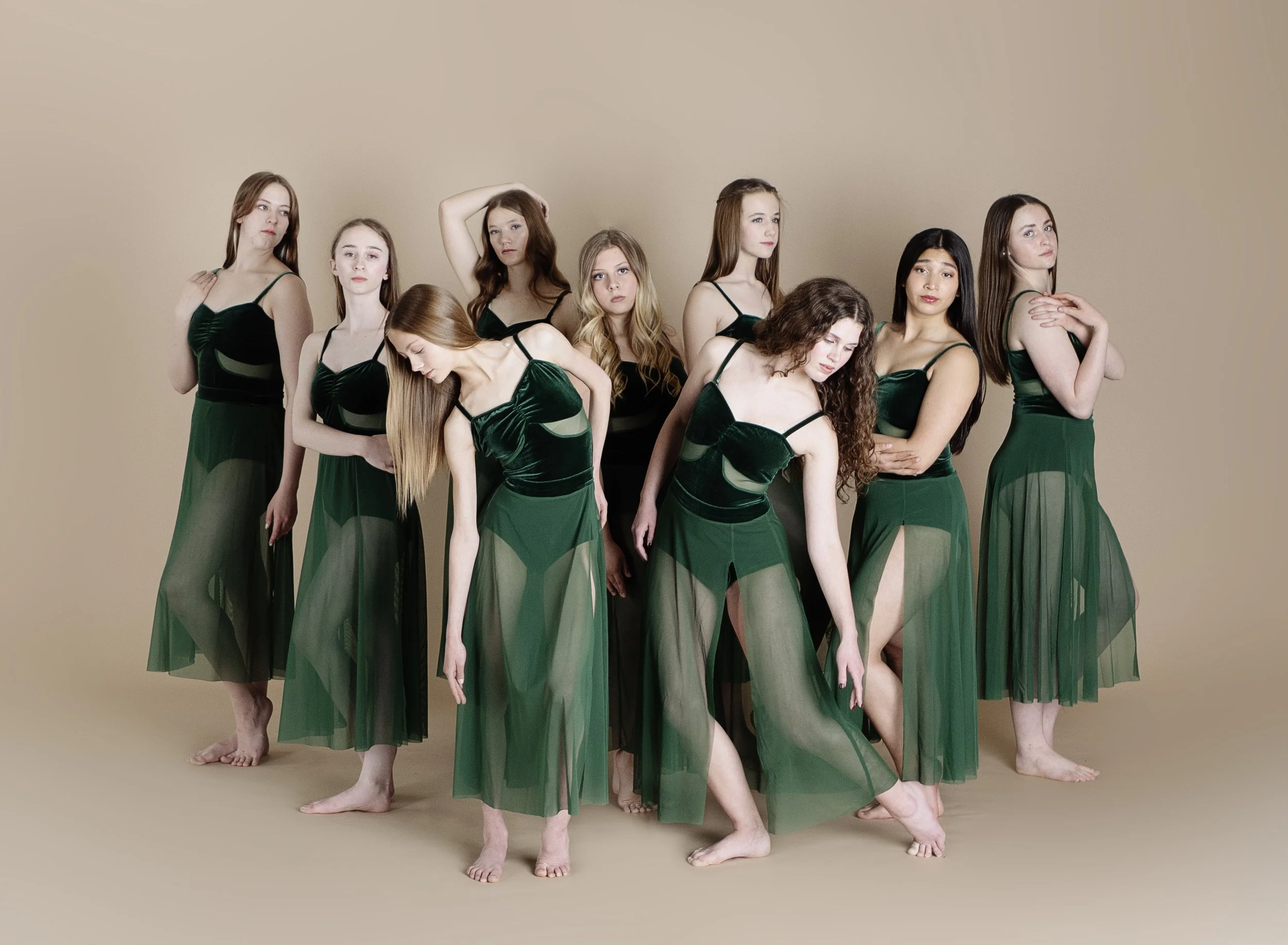 Ten young women in matching green dresses posing on a beige background.