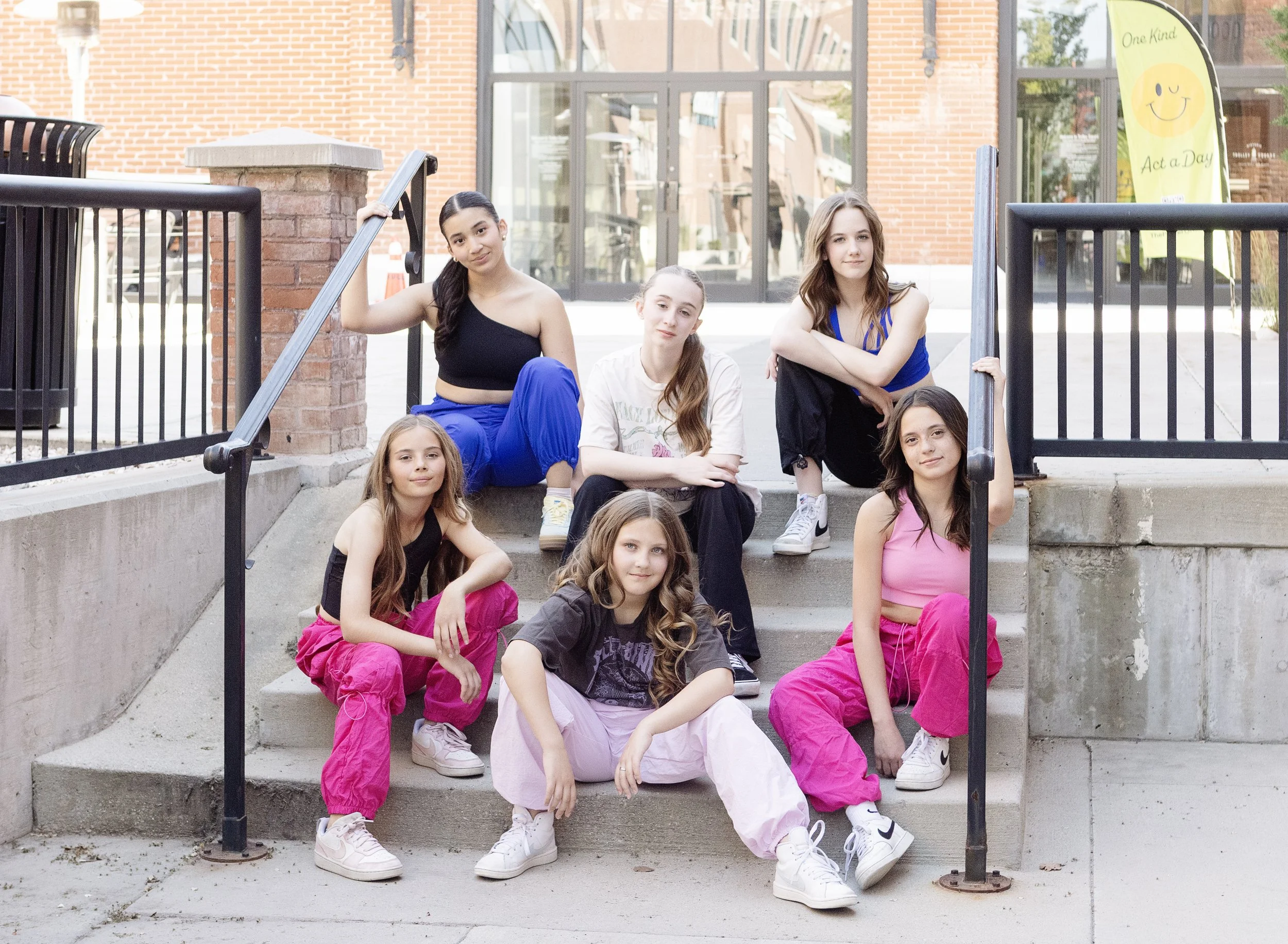Group of seven girls sitting on steps outside a building, posing for a photo.
