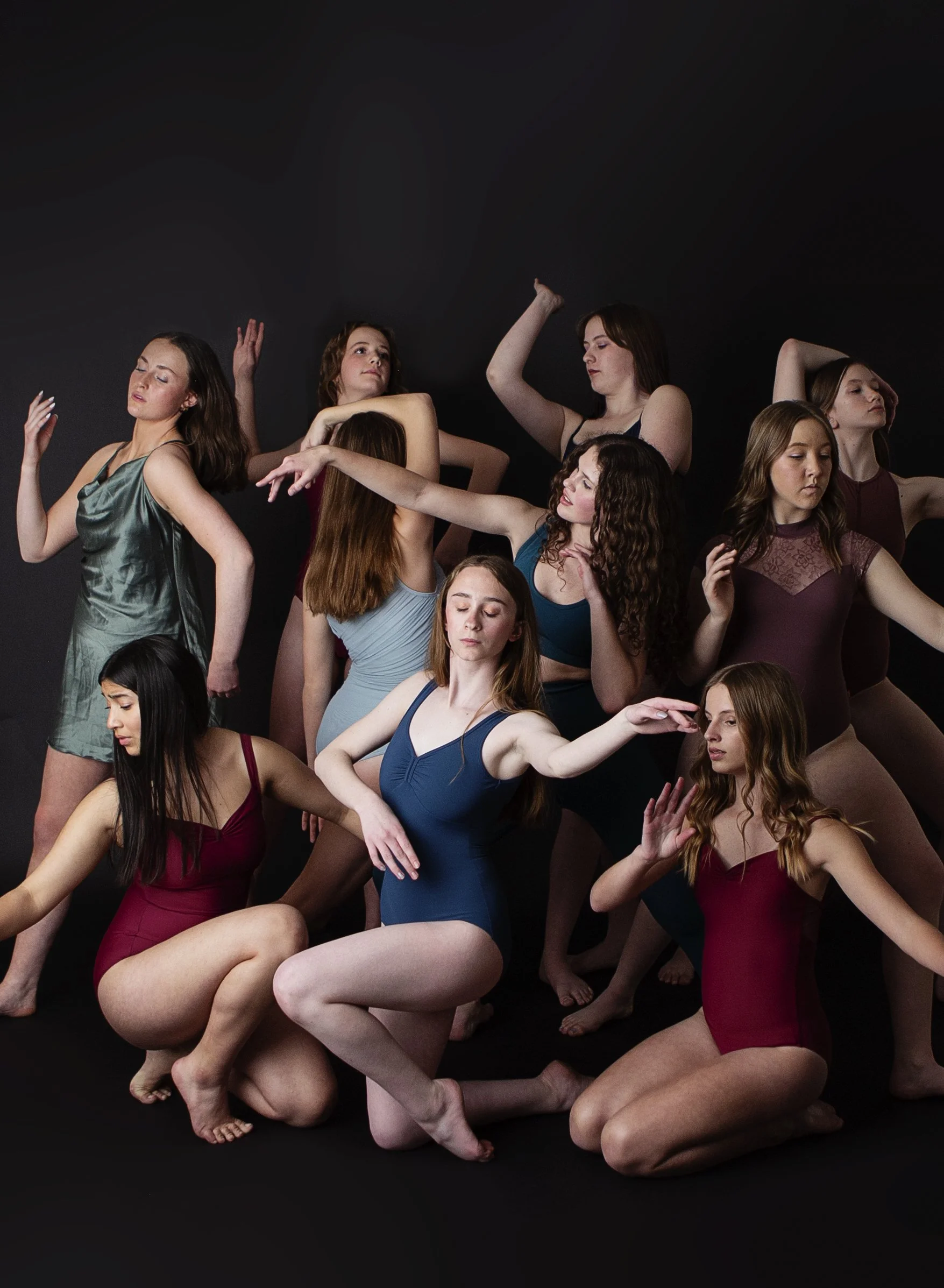 Group of young women in dance poses wearing colorful leotards against a black background.