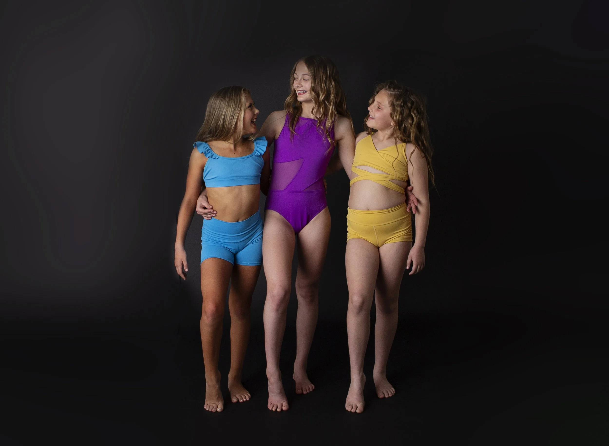 Three young girls wearing colorful dance outfits walking together and smiling.