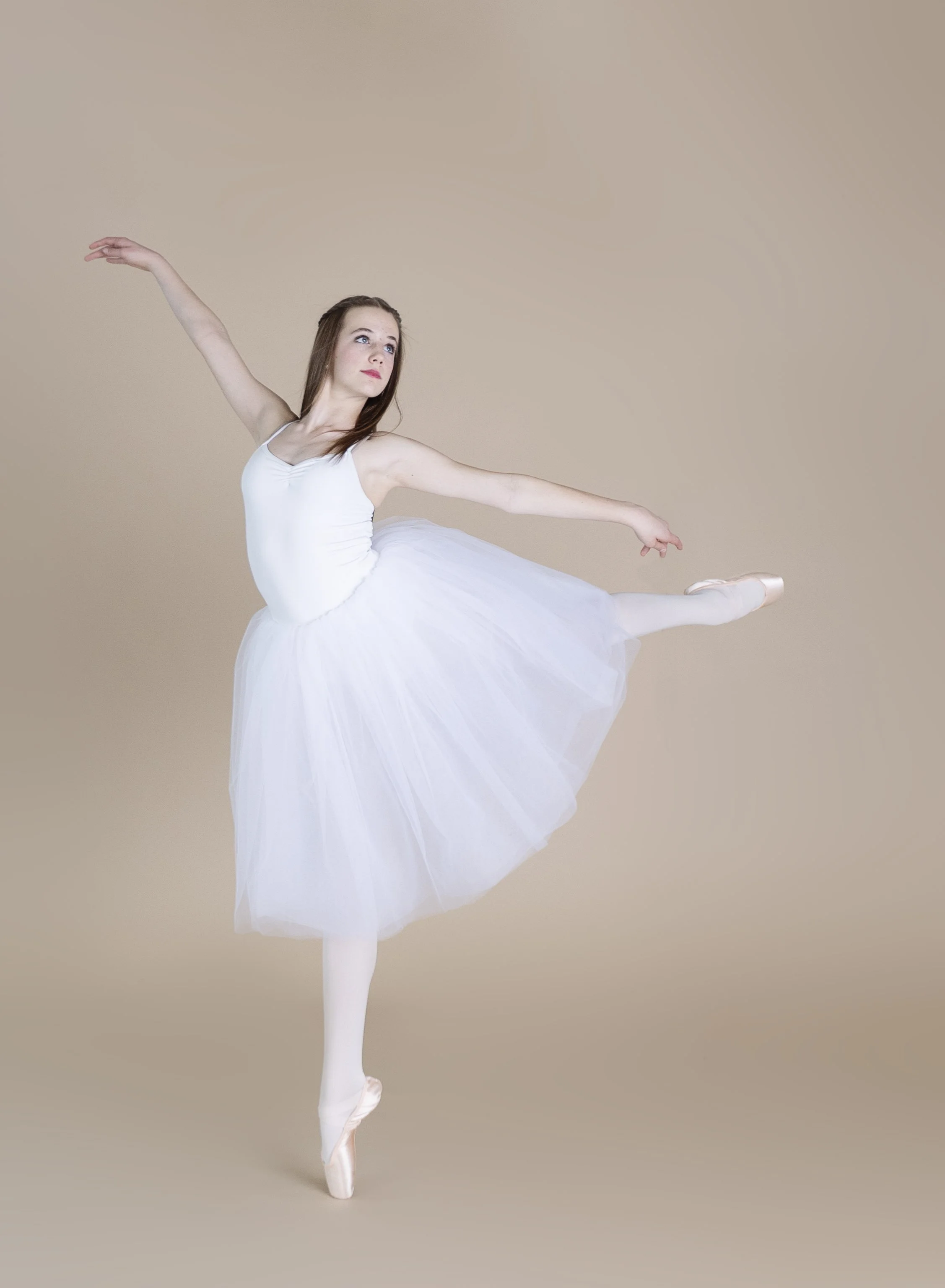 Ballet dancer in a white tutu performing a pose on pointe against a beige background.