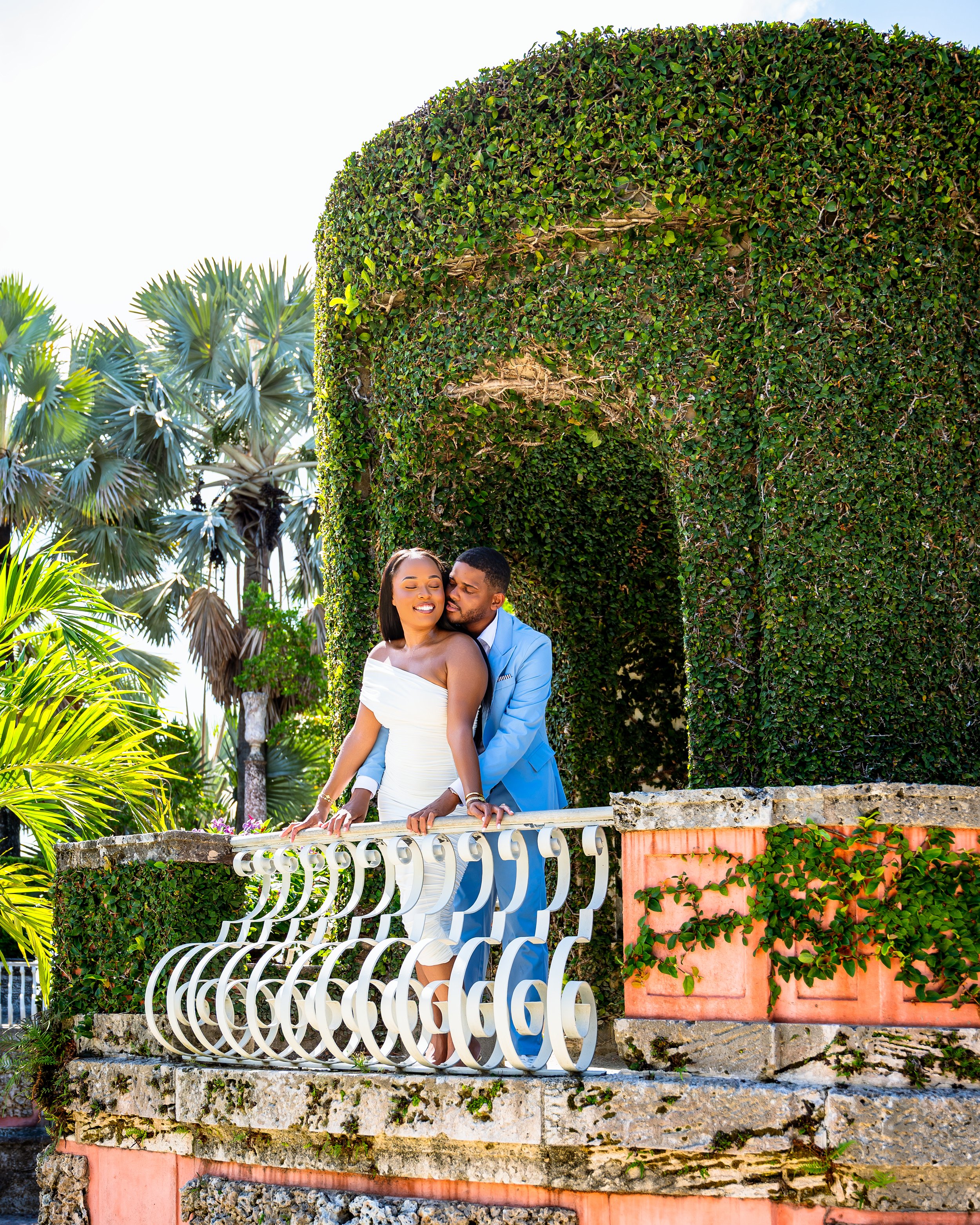 A couple embracing outdoors, with the man gently holding the woman's face and their noses touching, eyes closed, in a tender moment.