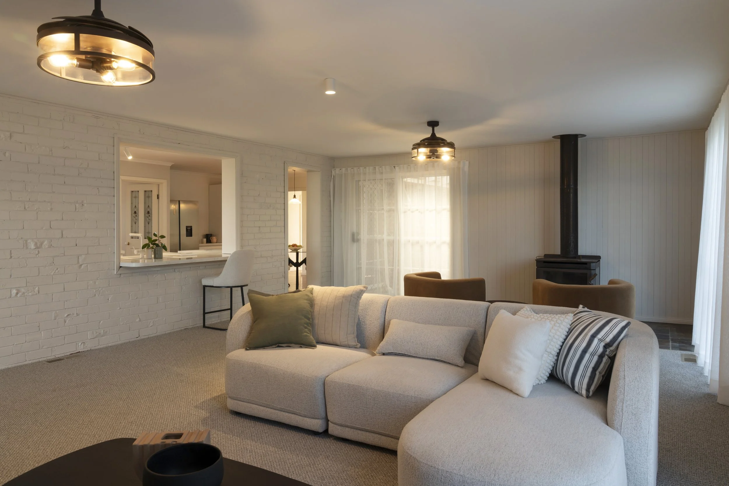 Large living room with neutral walls, consistent flooring, fireplace, soft furnishings and natural light in renovated Gisborne home.