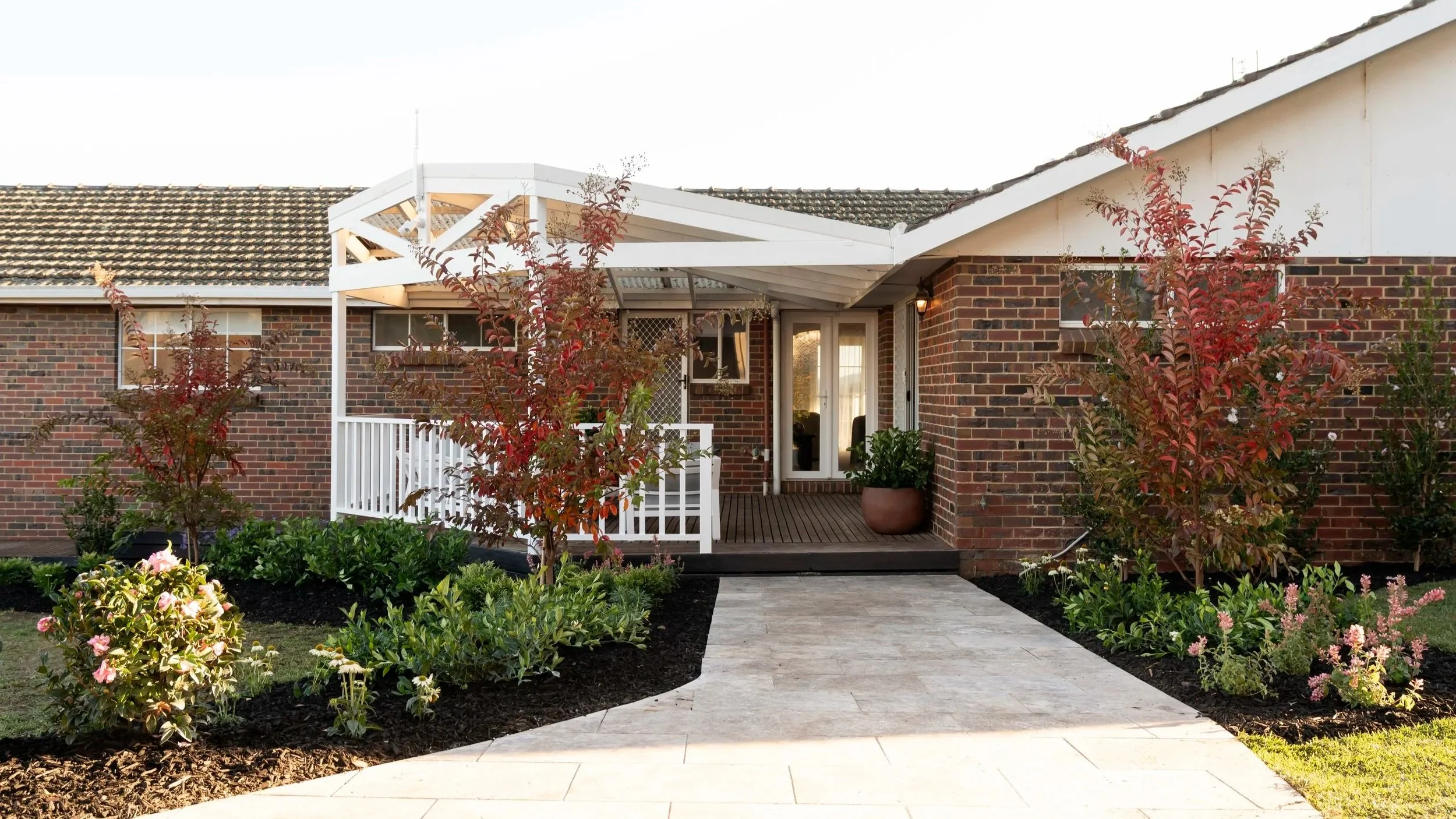Wide country-style entrance with gravel path, landscaped cottage garden, neutral exterior and defined front veranda in Gisborne Victoria home.