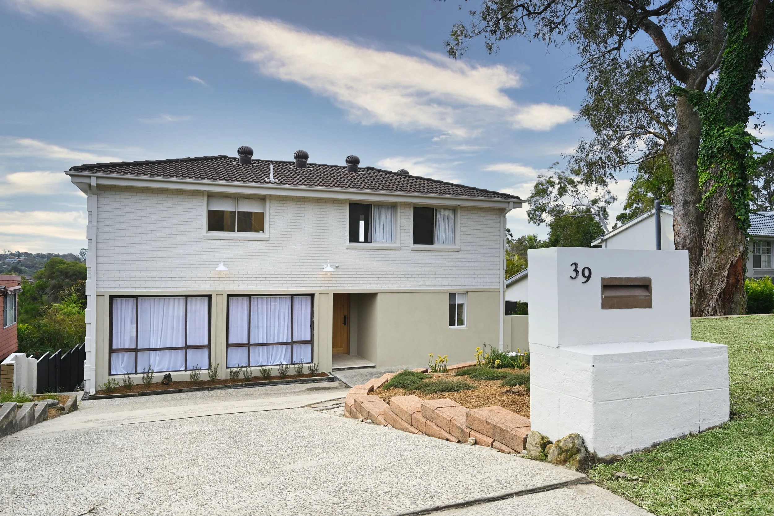 After: Fully refreshed facade with sandy render, cohesive colour scheme, tidy gardens, and updated lighting