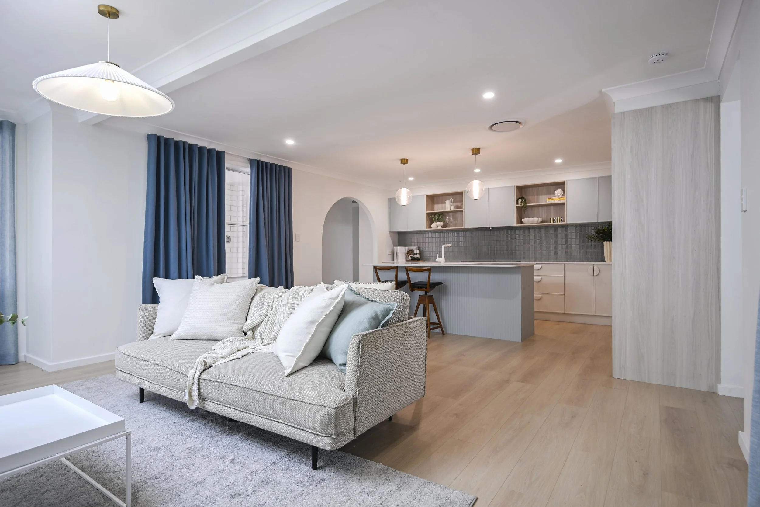 Calm, bright living and kitchen with layered lighting and coastal styling