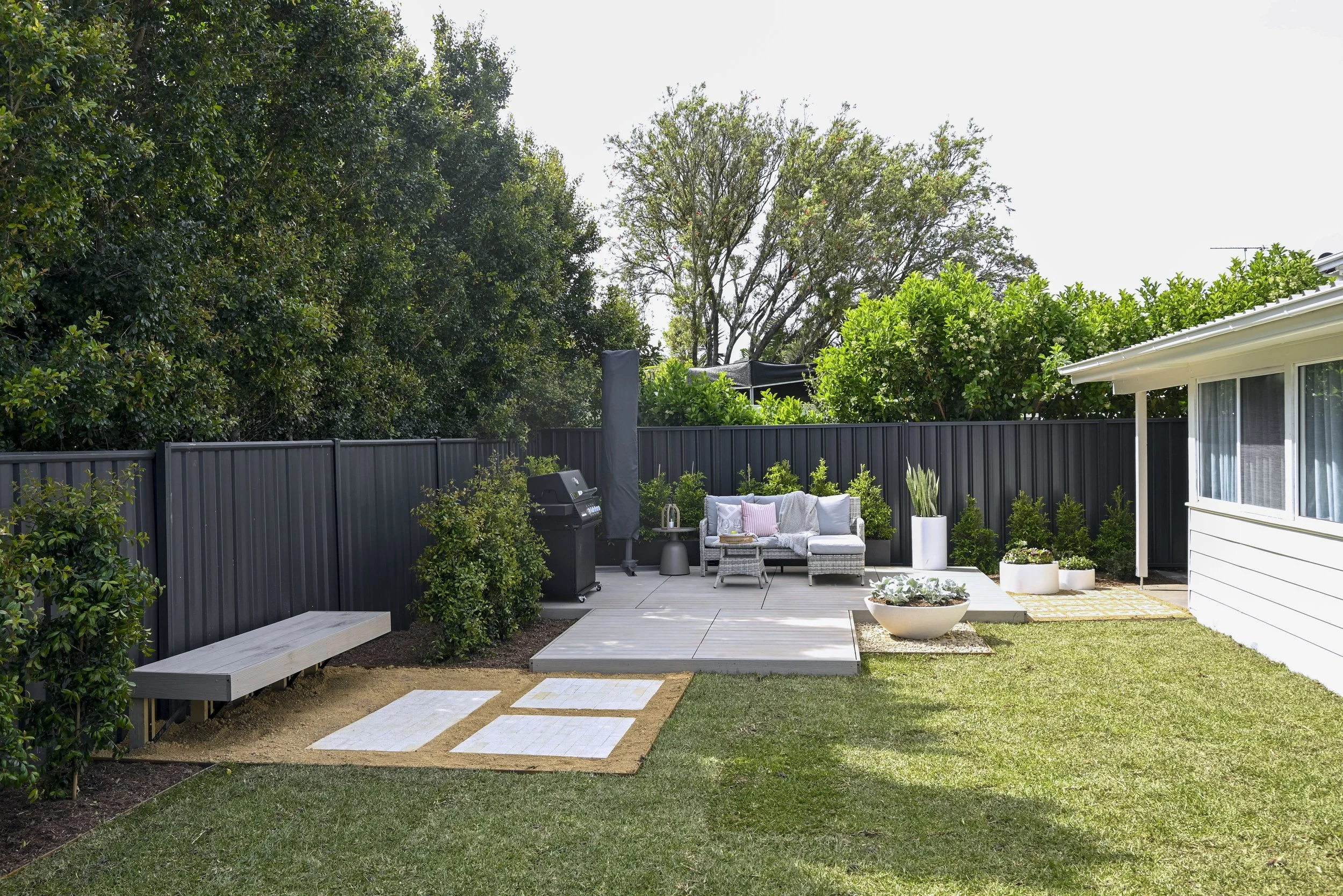 A zoned backyard with bright green turf, dark fences and attractive paved areas.