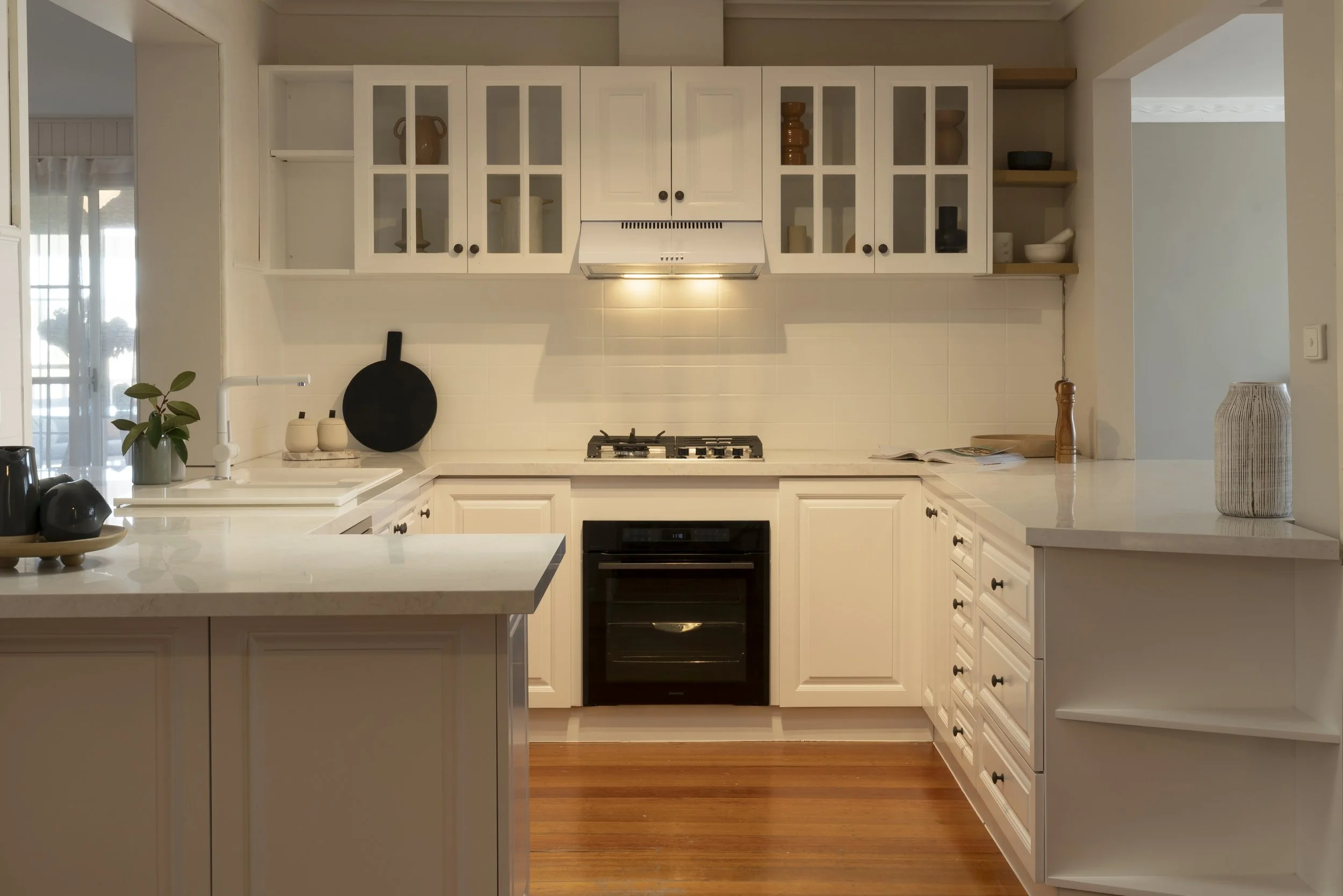 Country-style kitchen with white cabinets, Caesarstone benchtop, modern appliances and timber accents in Gisborne renovation.