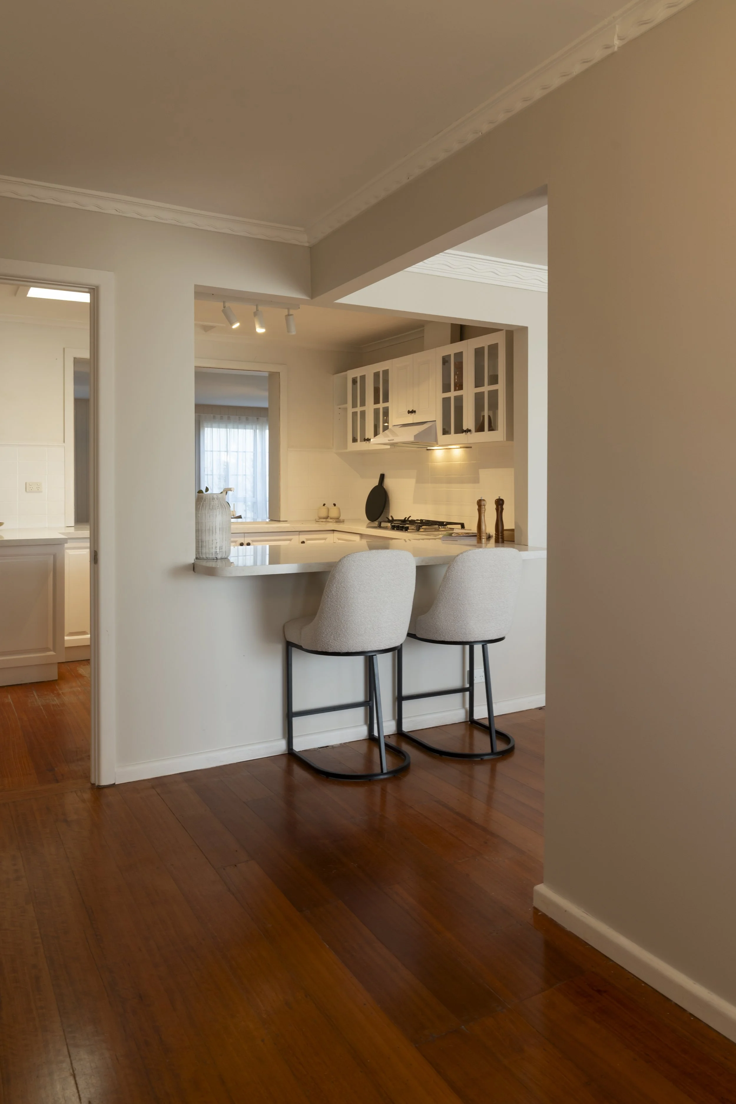 Stools at the island in a country-style kitchen with white cabinets and Caesarstone benchtops.