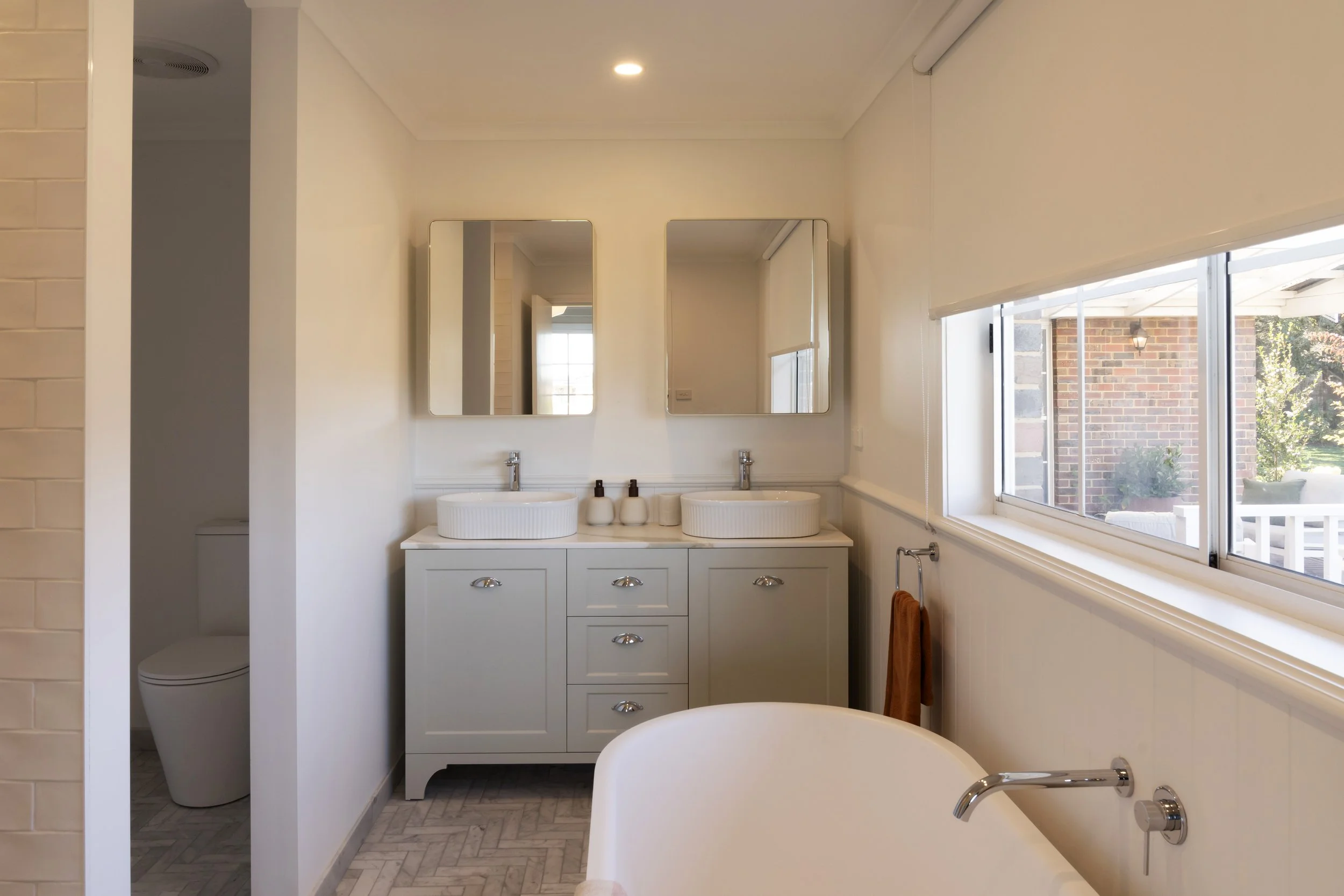 Large country-style ensuite bathroom with freestanding bath, double vanity, herringbone floor tiles and garden outlook.