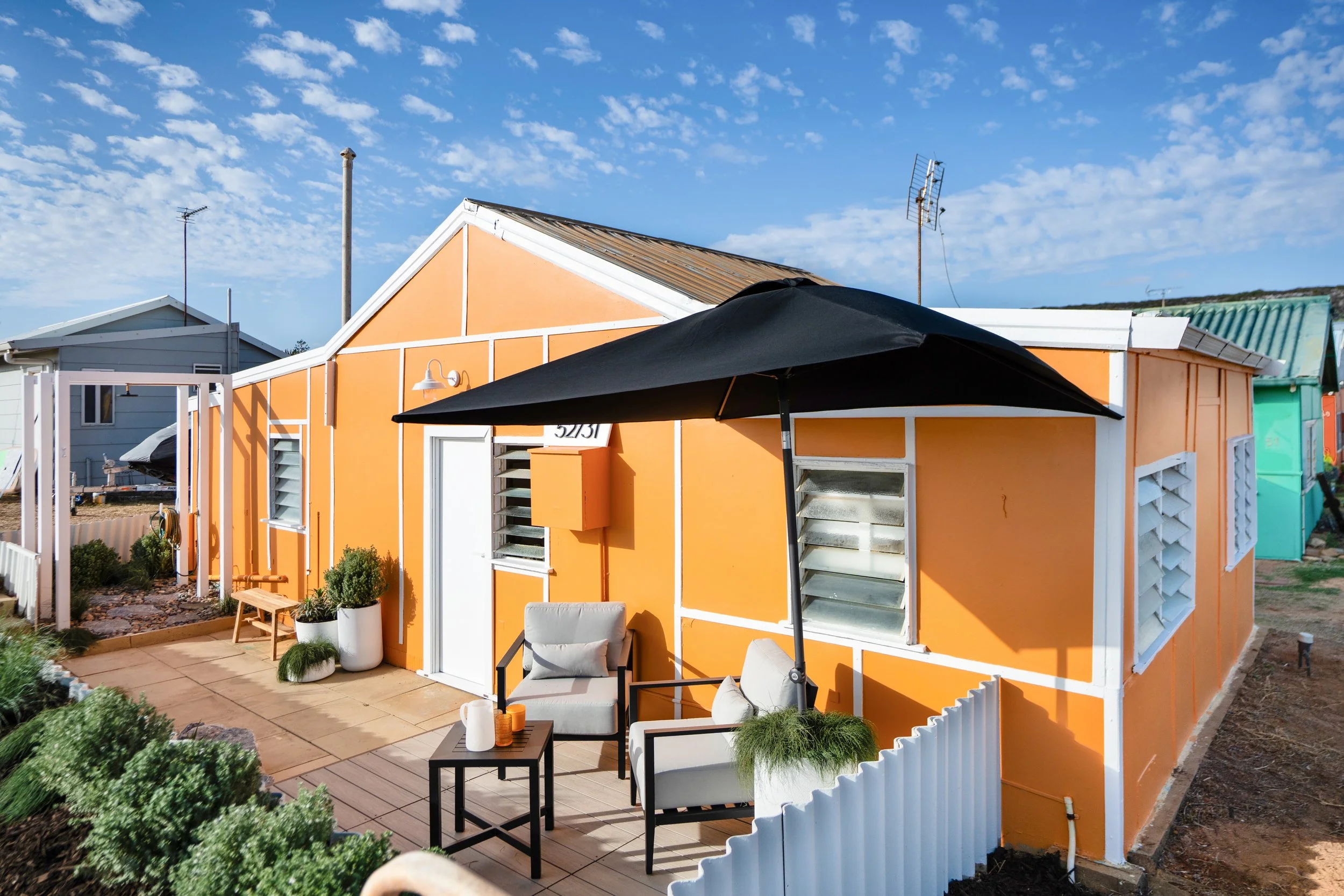 Vibrant tangerine‑coloured façade with white trim, raised deck, and lush coastal garden
